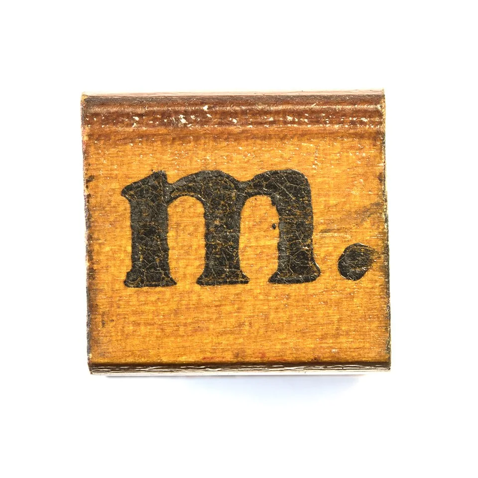 A wooden block with a black lowercase 'm' painted on it, with a period at the end, placed against a white background.