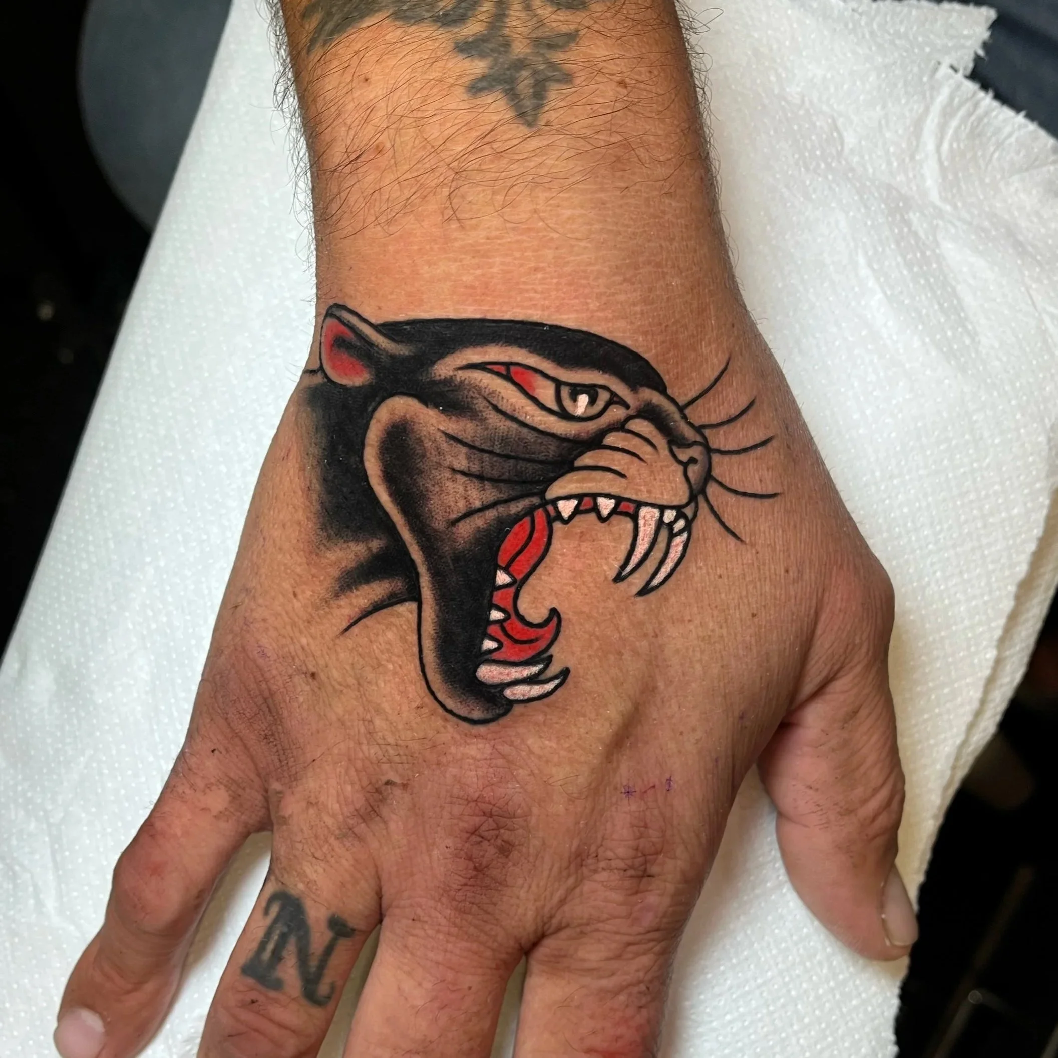 Tattoo of a roaring black panther with red accents, on a person's hand and wrist.