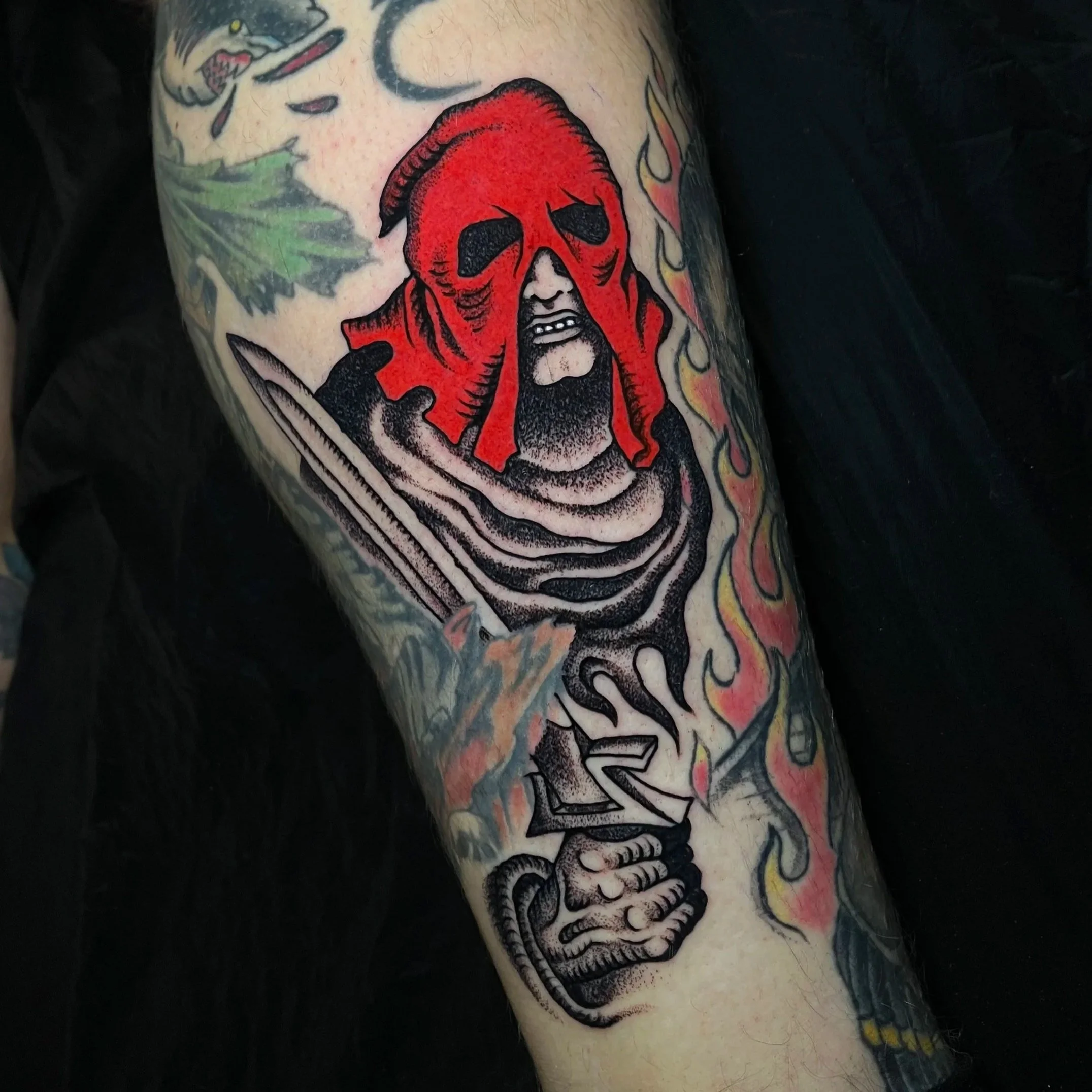 Tattoo of a grim reaper with a red hood and skull face holding a sword, surrounded by flames. Sodom tattoo