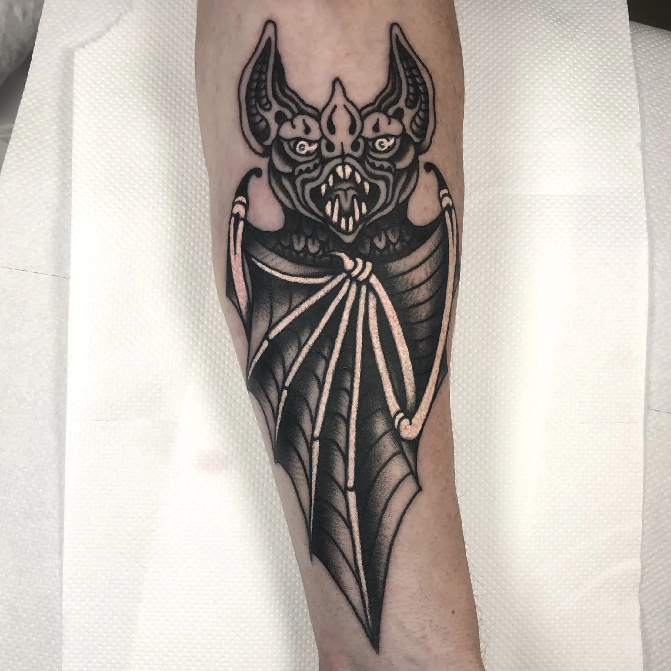 Black and gray tattoo of a dragon head with wings on a person's arm.