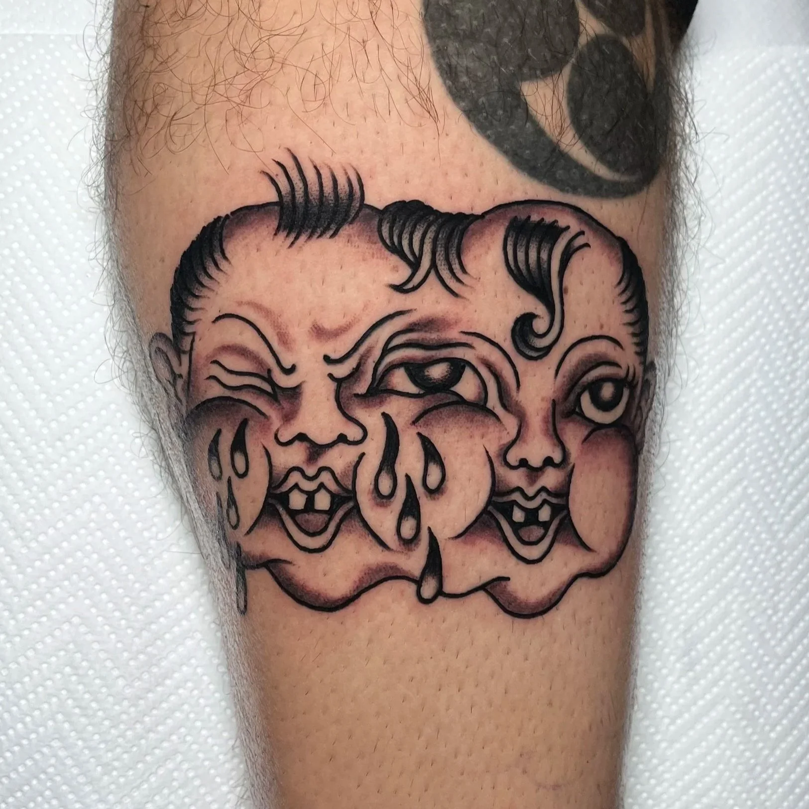 Tattoo of three clown faces with exaggerated features, tears, and dripping elements, in a traditional tattoo style.
