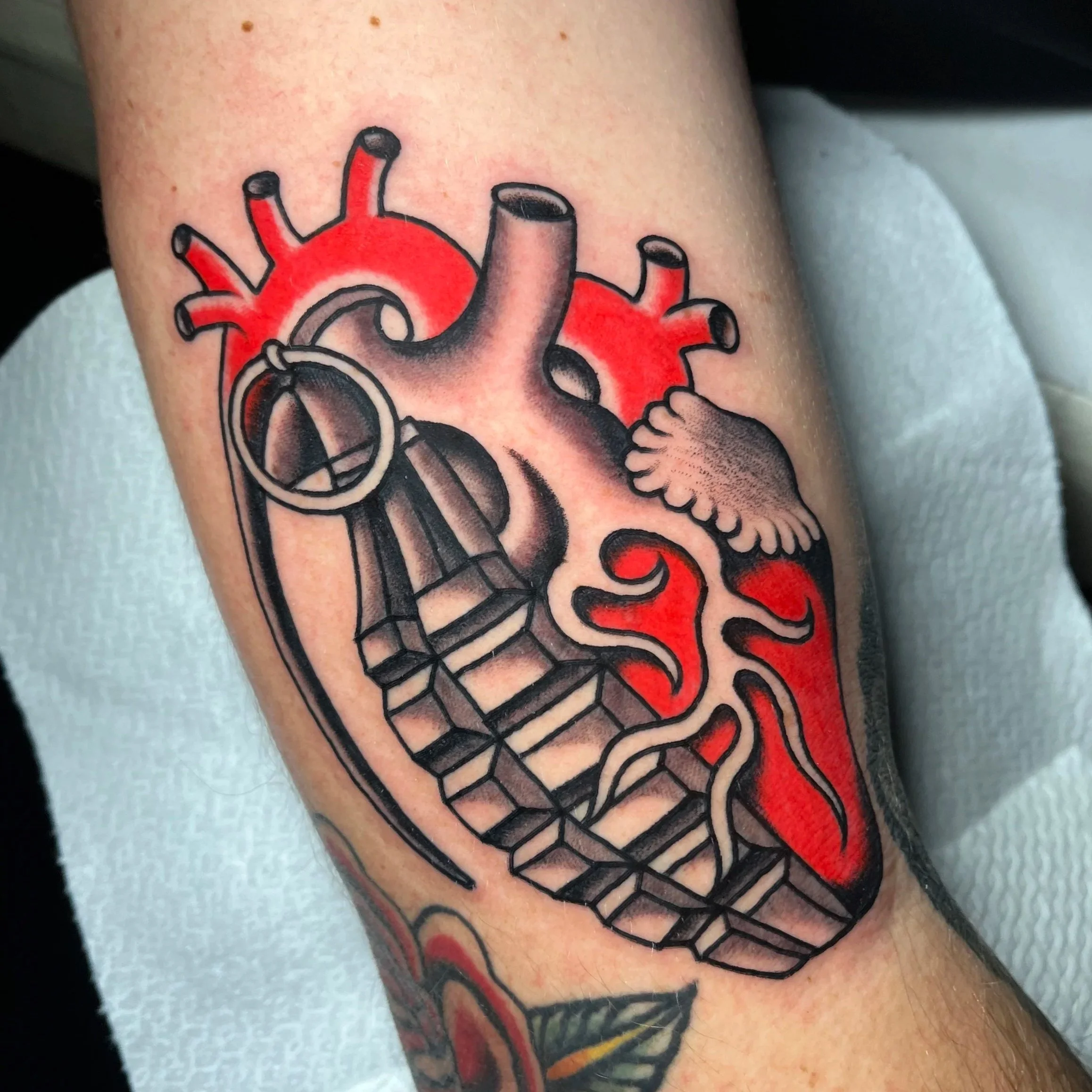 Tattoo of a stylized human heart with black outlines, red shading, and intricate details including coronary arteries and veins.