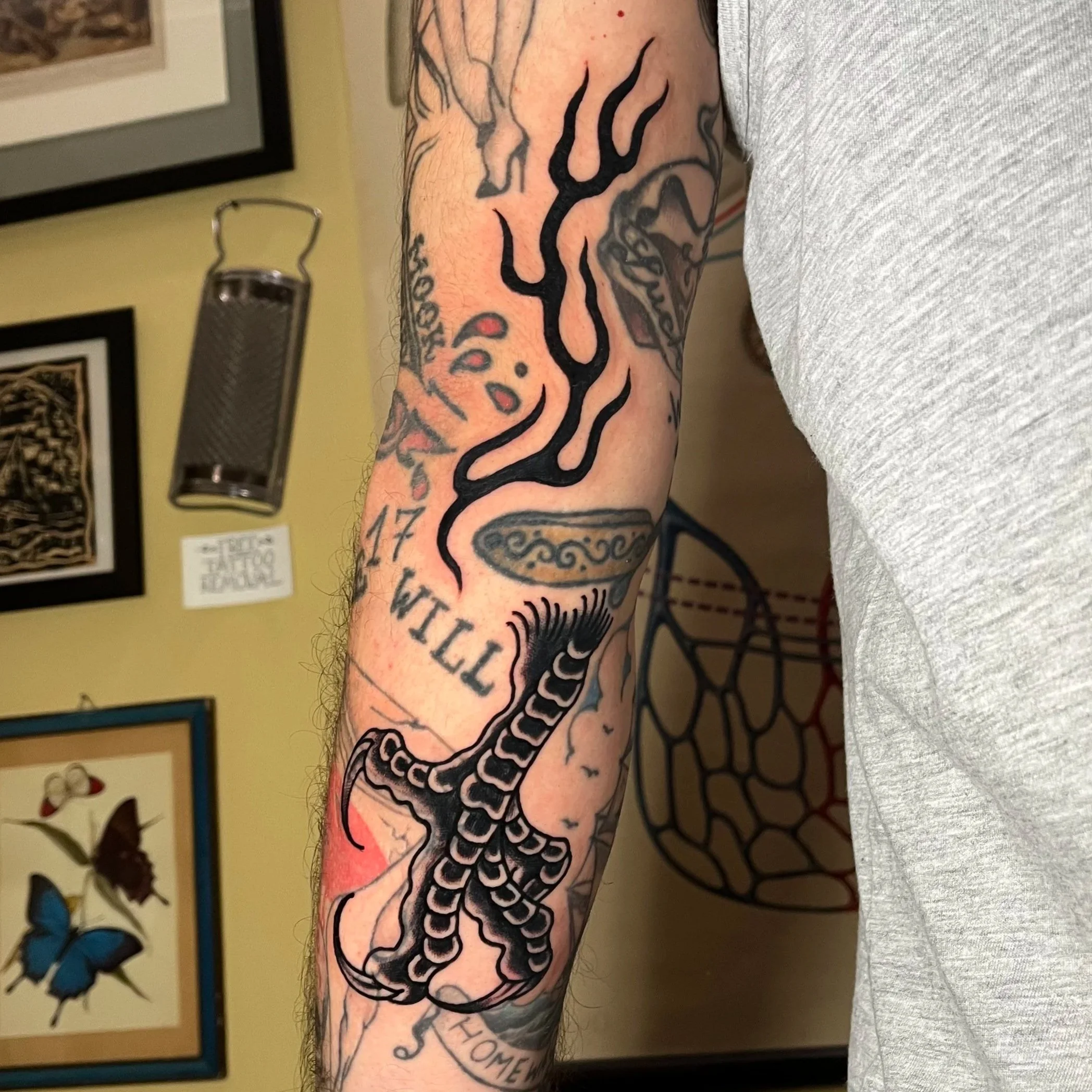 Tattoo of a smoking pipe, a snake, a banner with the text 'I TILL' and various other designs on a person's arm.