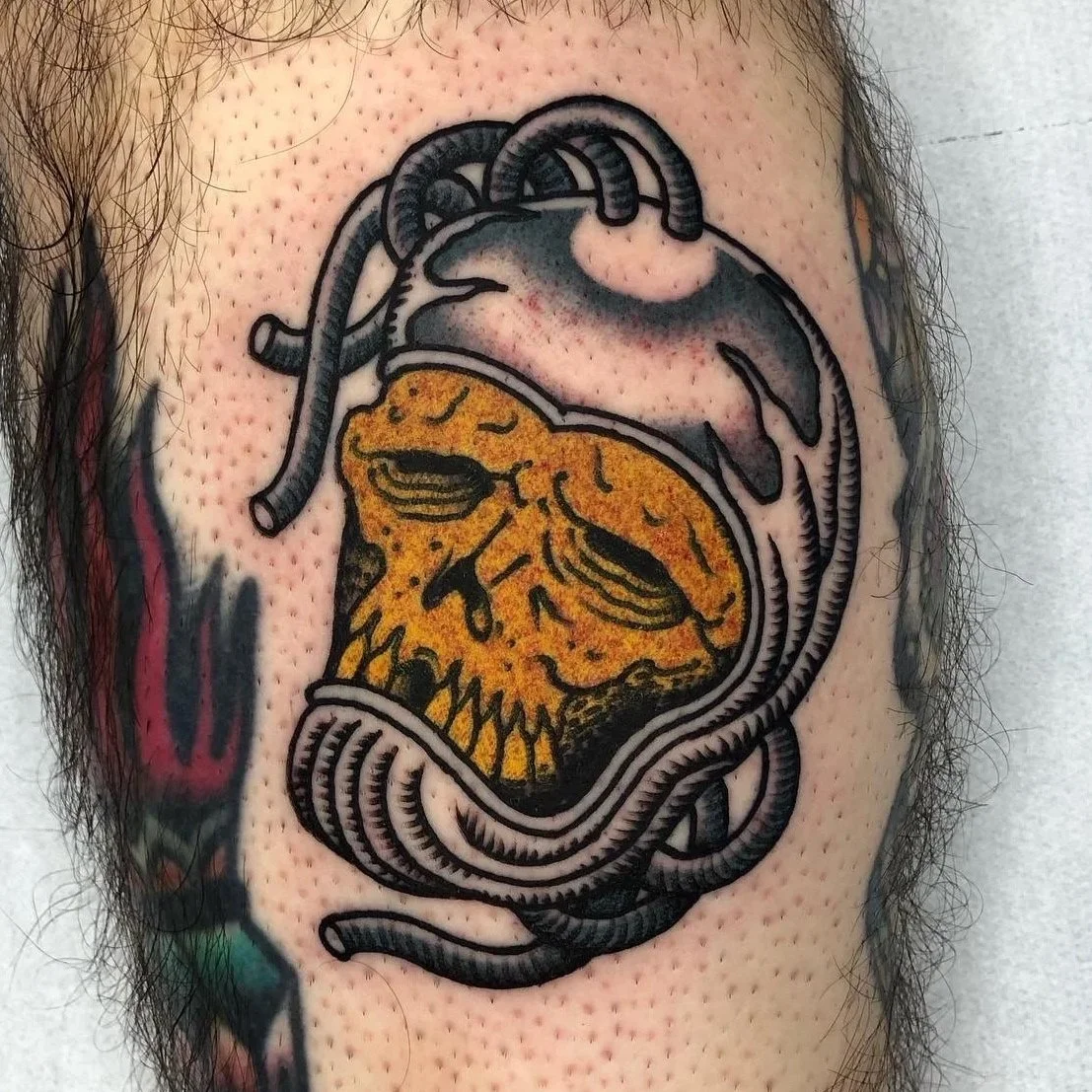 Tattoo of an anatomical heart with a yellow lion's face inside it, featuring bold black outlines and shading.