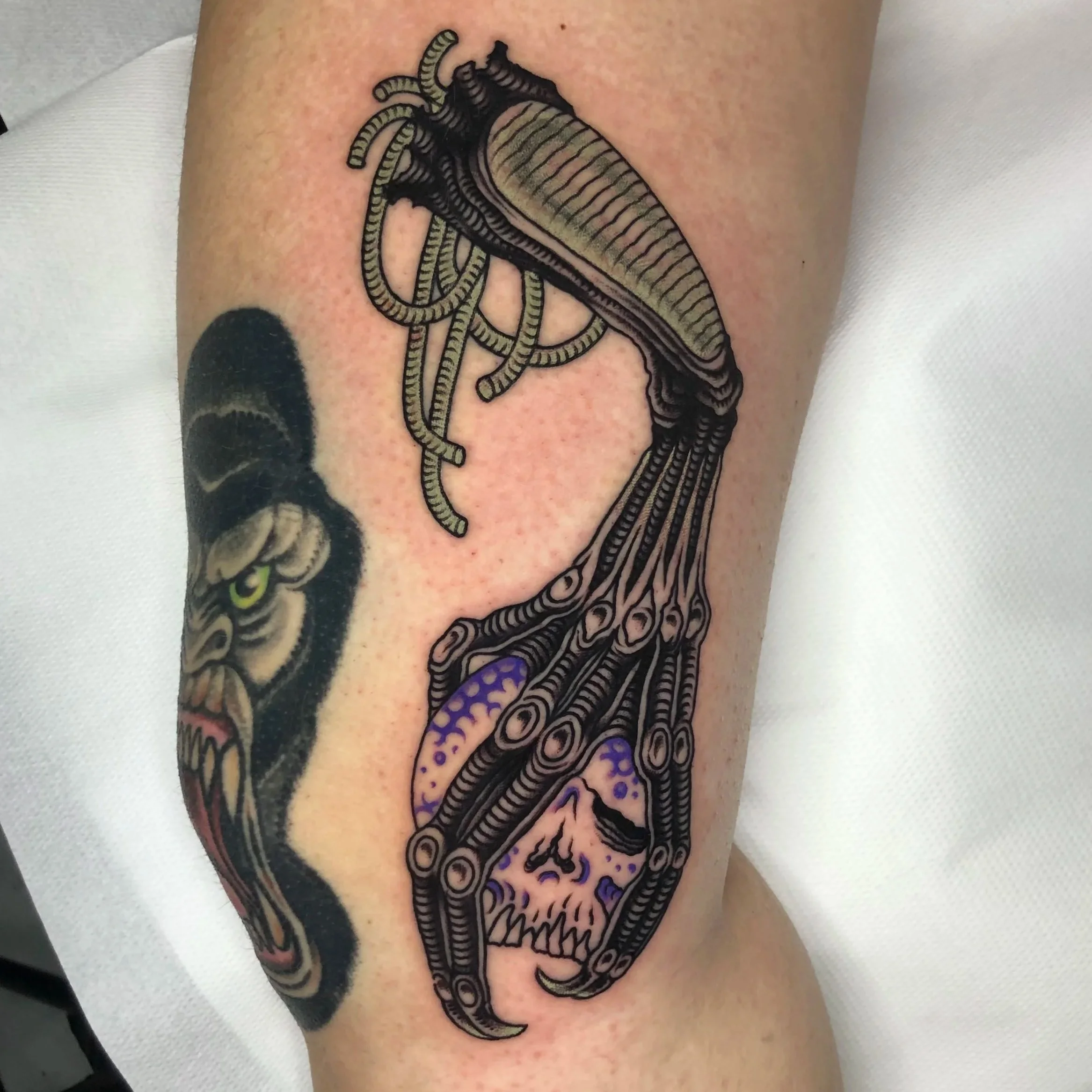 Tattoo of a mechanical style alien creature with tentacles and a skull on the arm.