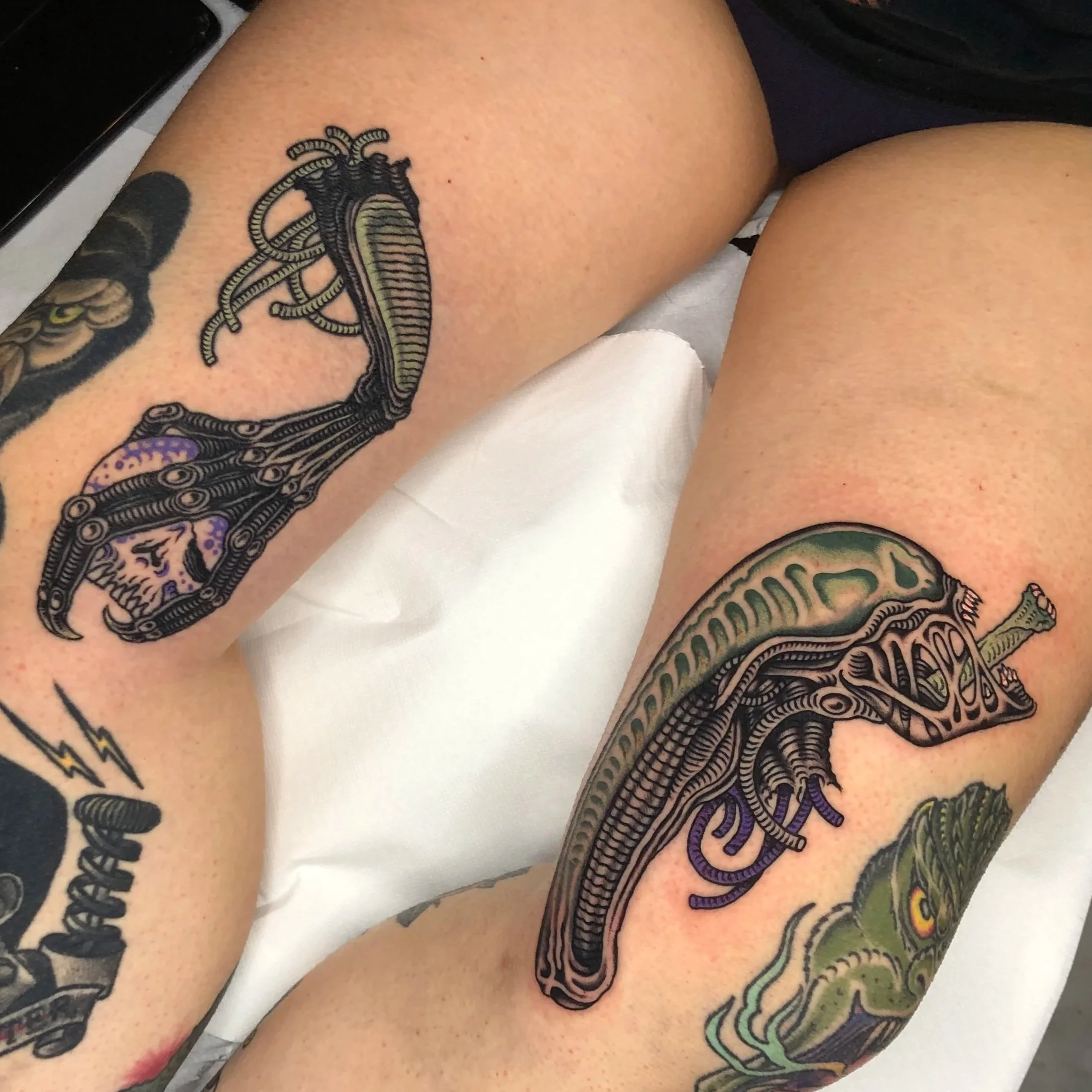 Colorful tattoos of biomechanical and fantasy creatures on person's thighs.