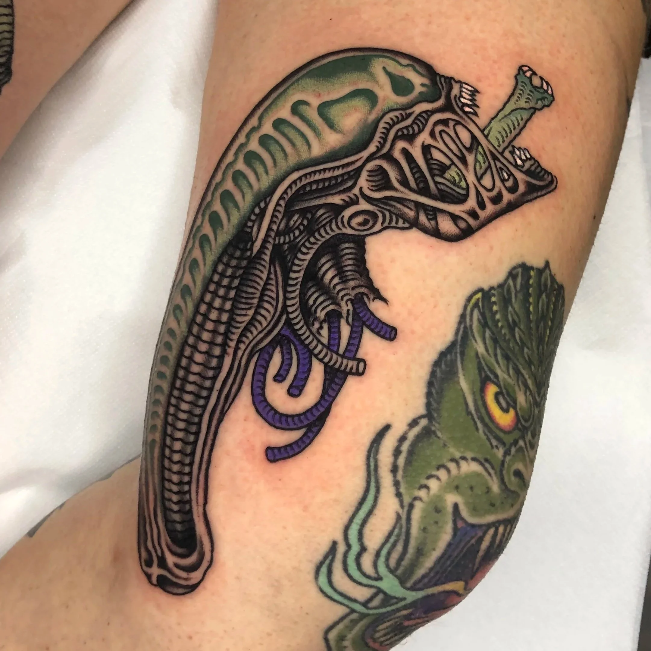 Colorful tattoo of alien on a person's leg, with intricate black lines and purple accents.