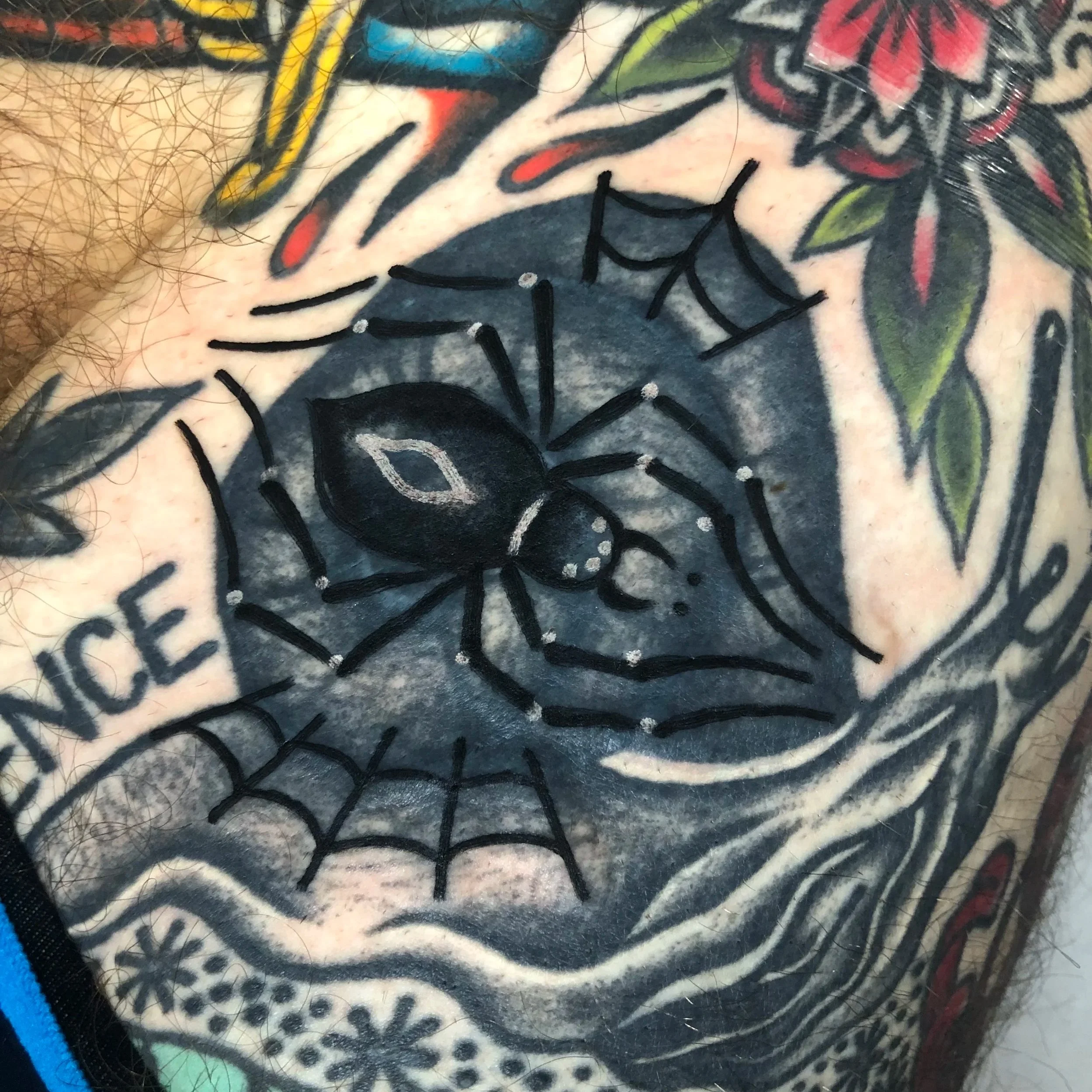 Tattoo of a black widow spider with a web on a person's chest, surrounded by floral and text elements.