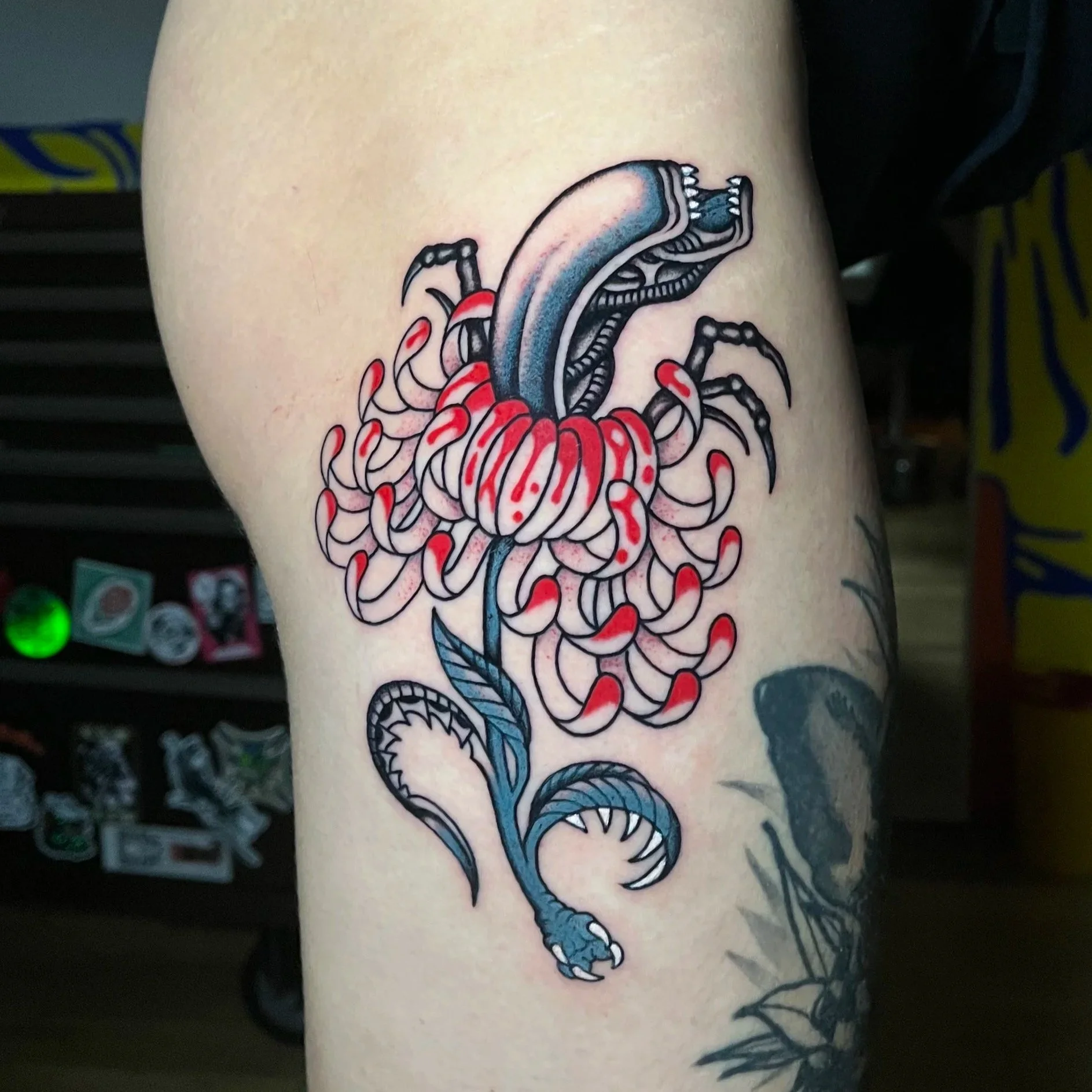 Tattoo of a stylized, colorful alien with a crab-like body and a long tongue, with a large bug or worm emerging from its mouth.