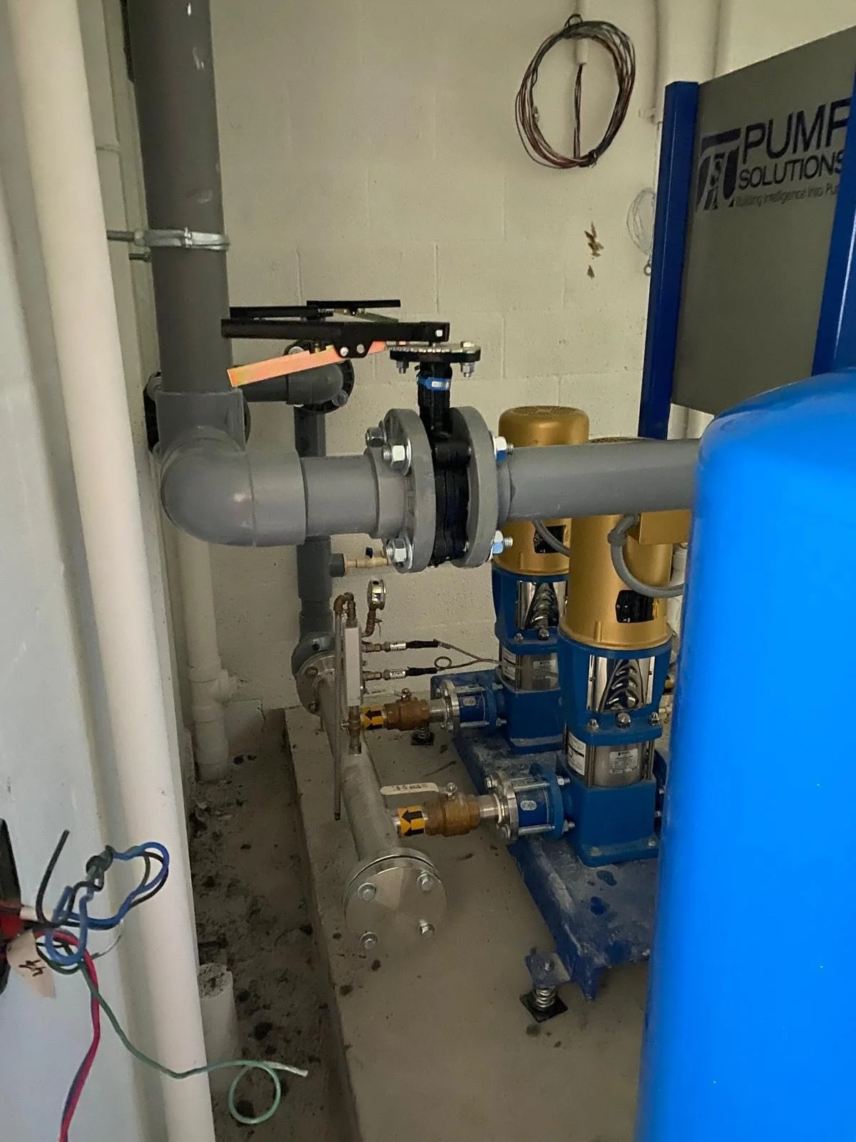 Industrial plumbing system with large gray pipes, valves, and blue and yellow equipment in a utility room.