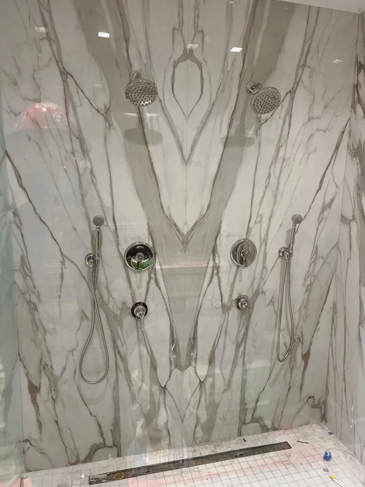 Two showerheads and two handheld shower wands in a marble wall shower.