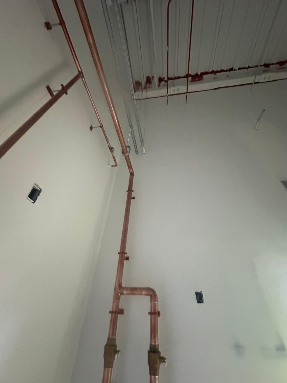 Copper pipes installed on a wall and ceiling of a building under construction or renovation.