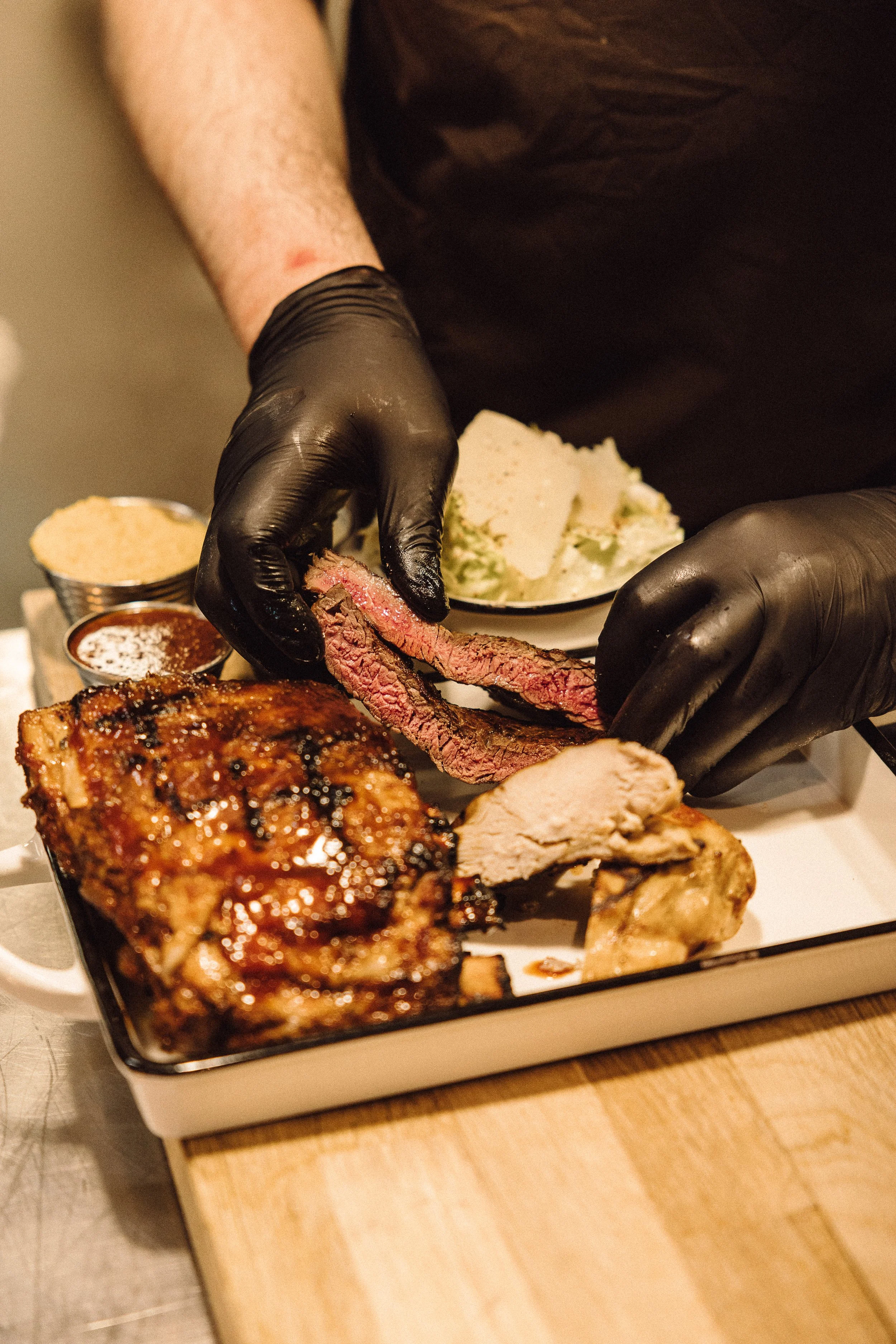 Person slicing cooked beef brisket with a chef's knife at a BBQ meal with sides on a tray.