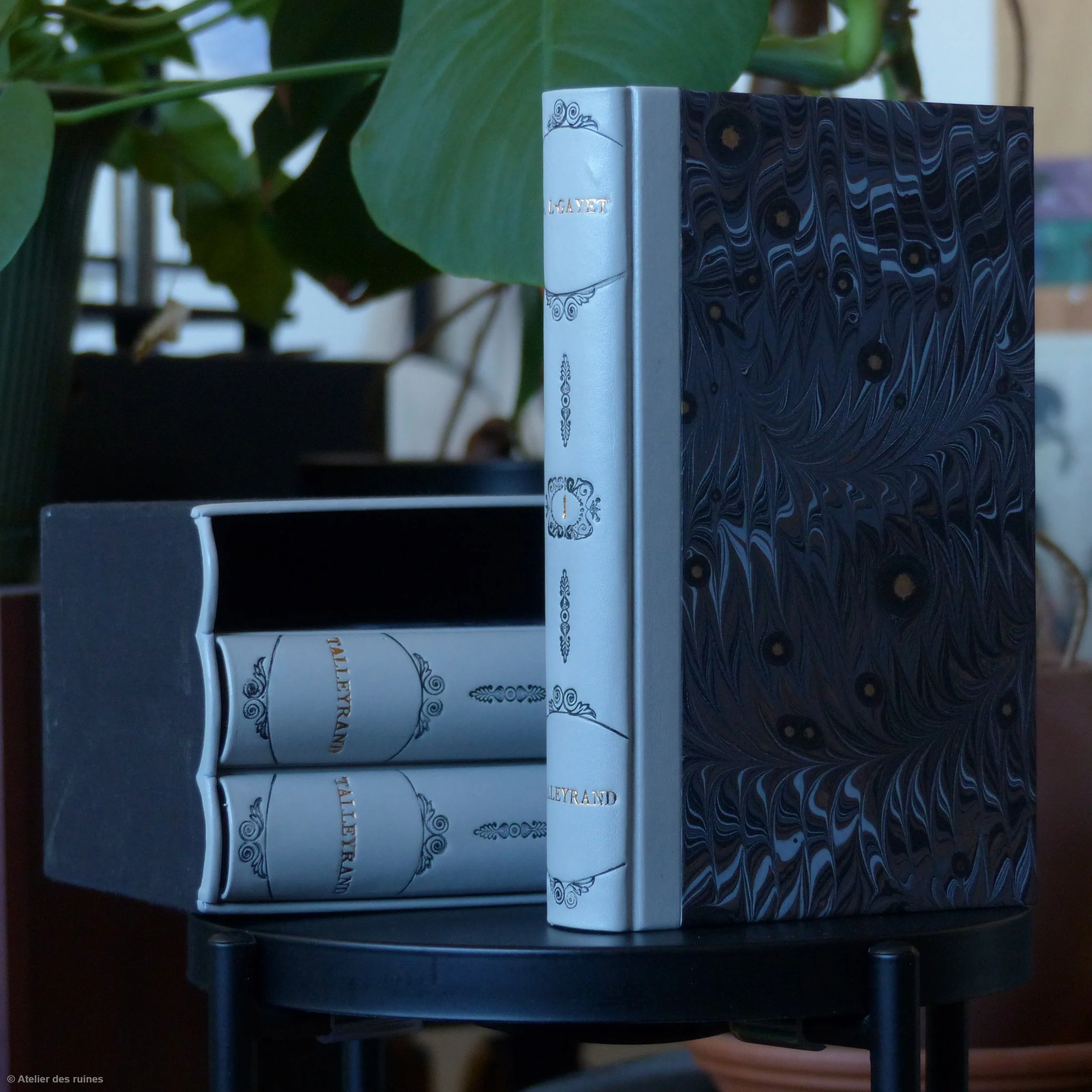 Une pile de livres avec des couvertures décoratives, placés contre un mur ou une surface sombre. On distingue la tranche de plusieurs livres, certains avec des motifs marbrés ou ornés.