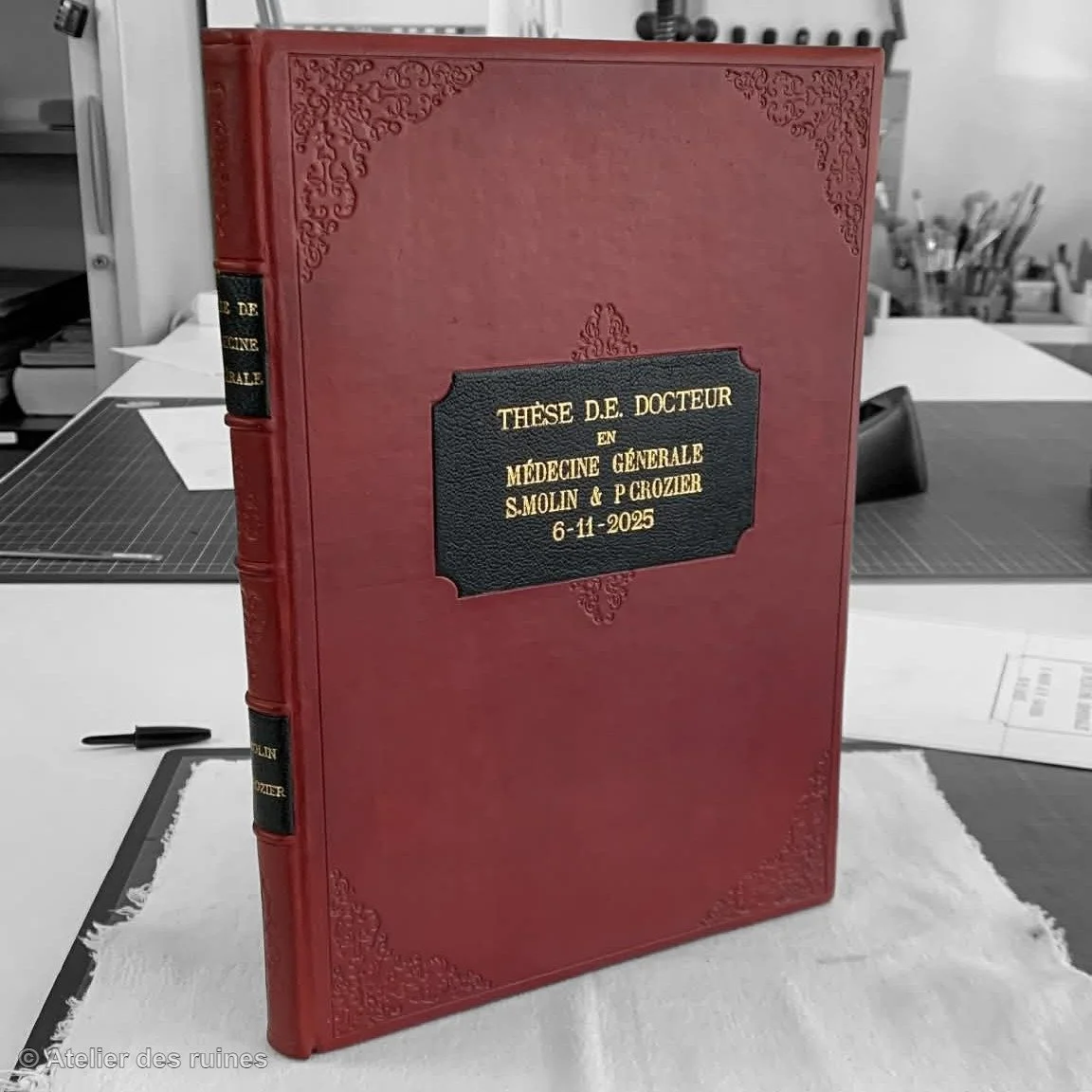 Un livre rouge avec une reliure décorative, intitulé en français : 'Thèse D.E. Docteur en Médecine Générale S. Molin & P. Crozier 6-11-2025'.