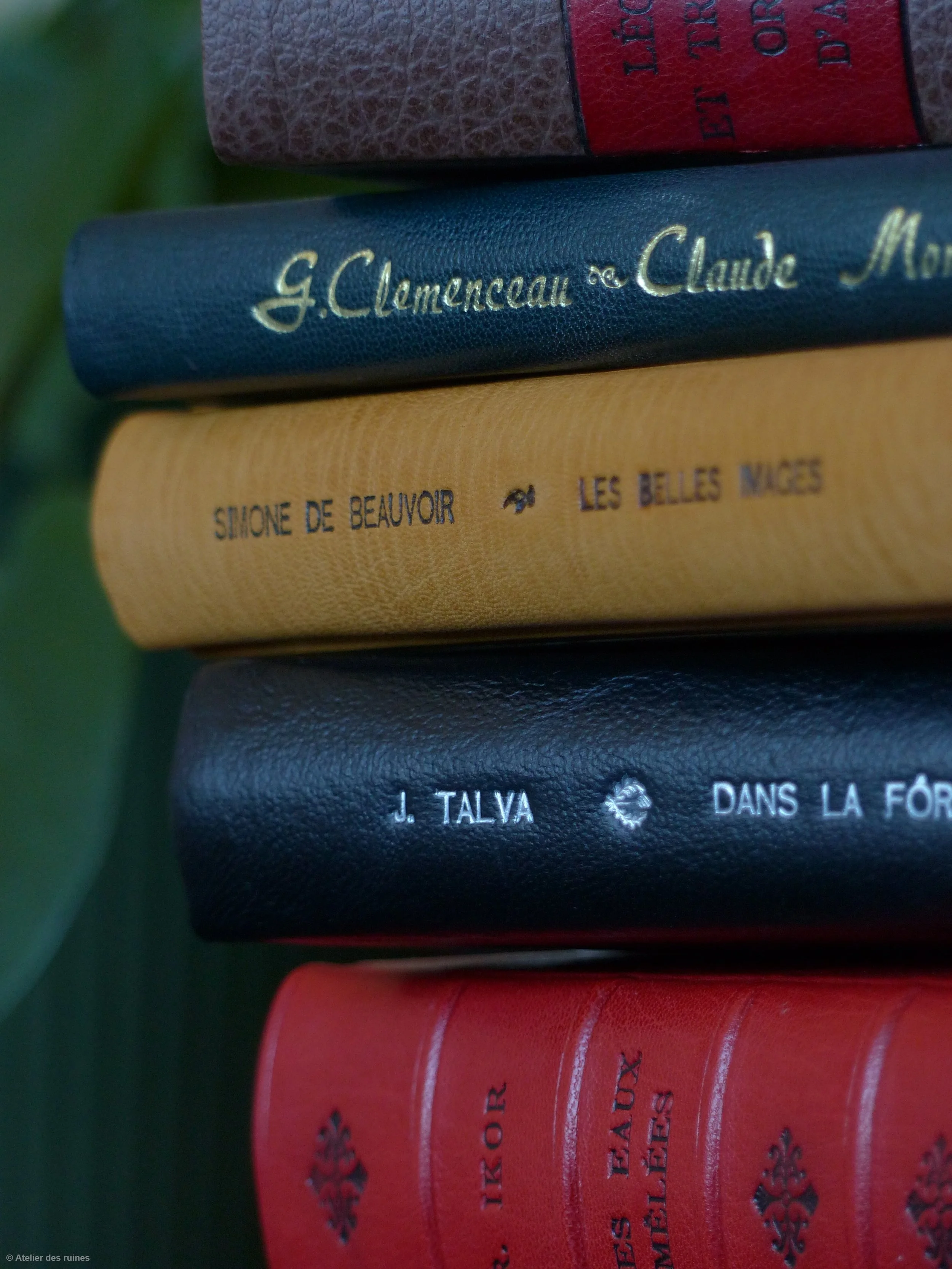 Trois livres empilés, avec des couvertures colorées et des titres en français, sur une surface en bois ou autre matériau foncé.