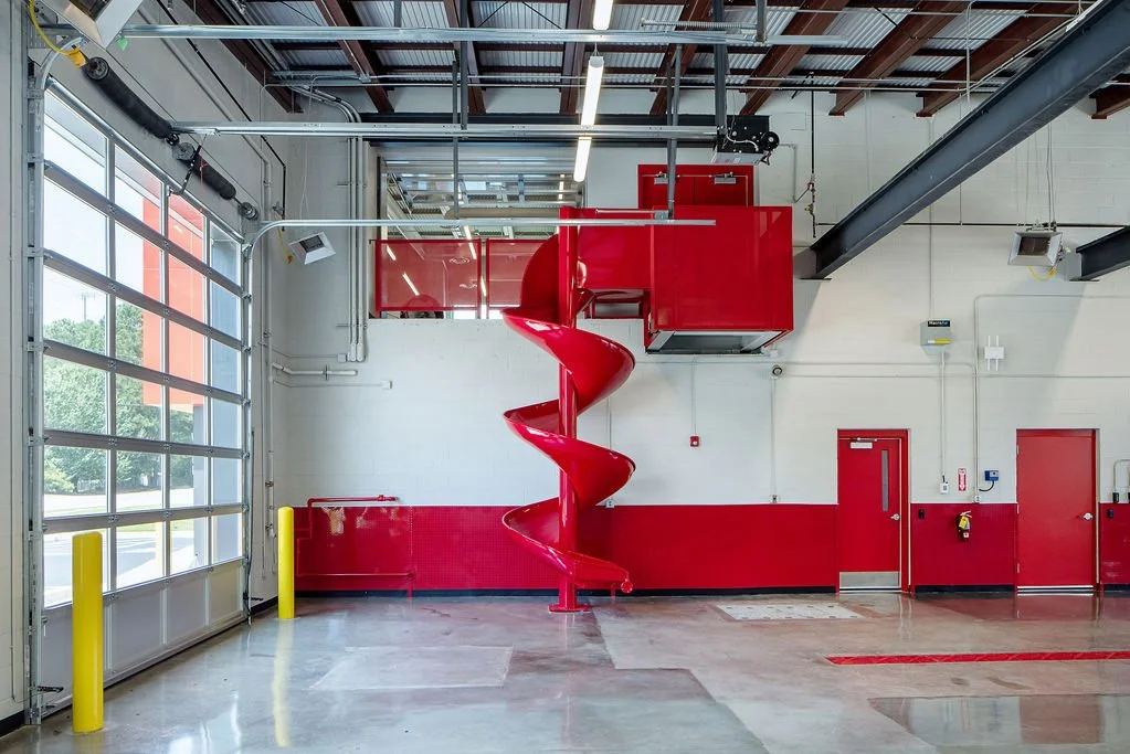 Empty industrial garage with a bright red spiral slide, large garage door, and fire safety equipment.