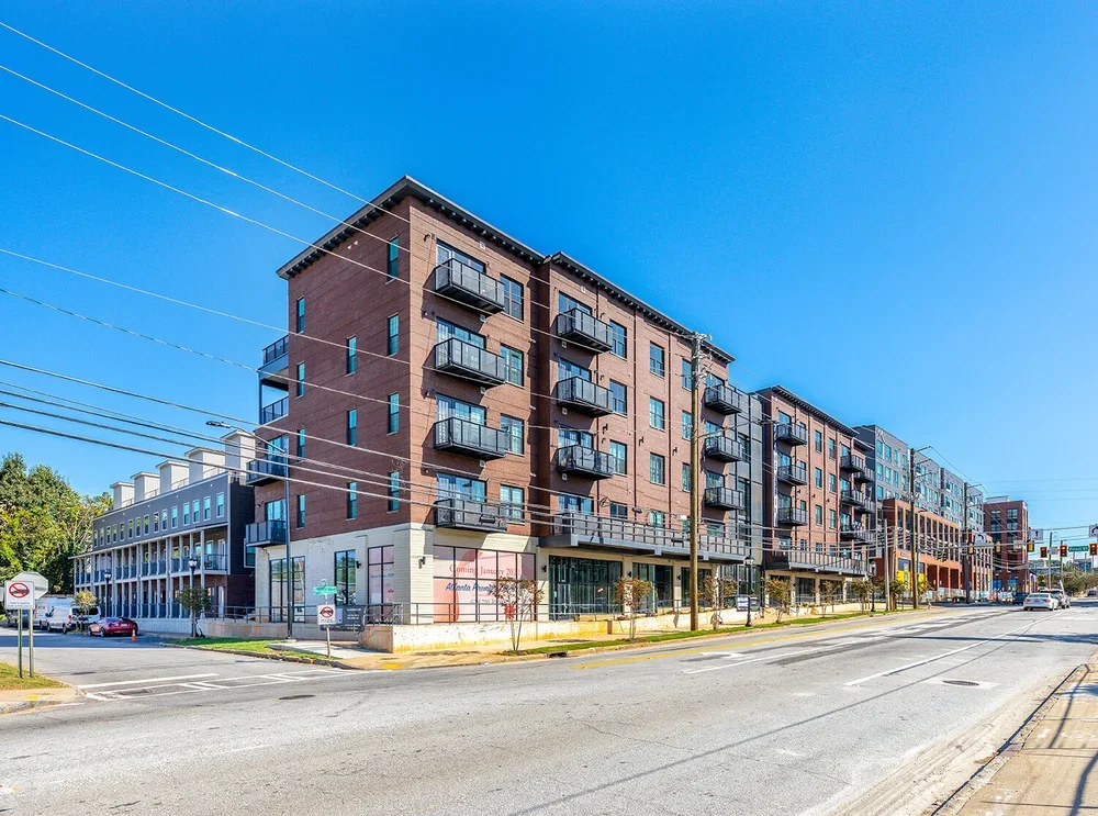 A modern multi-story apartment building on a city street with clear blue sky.