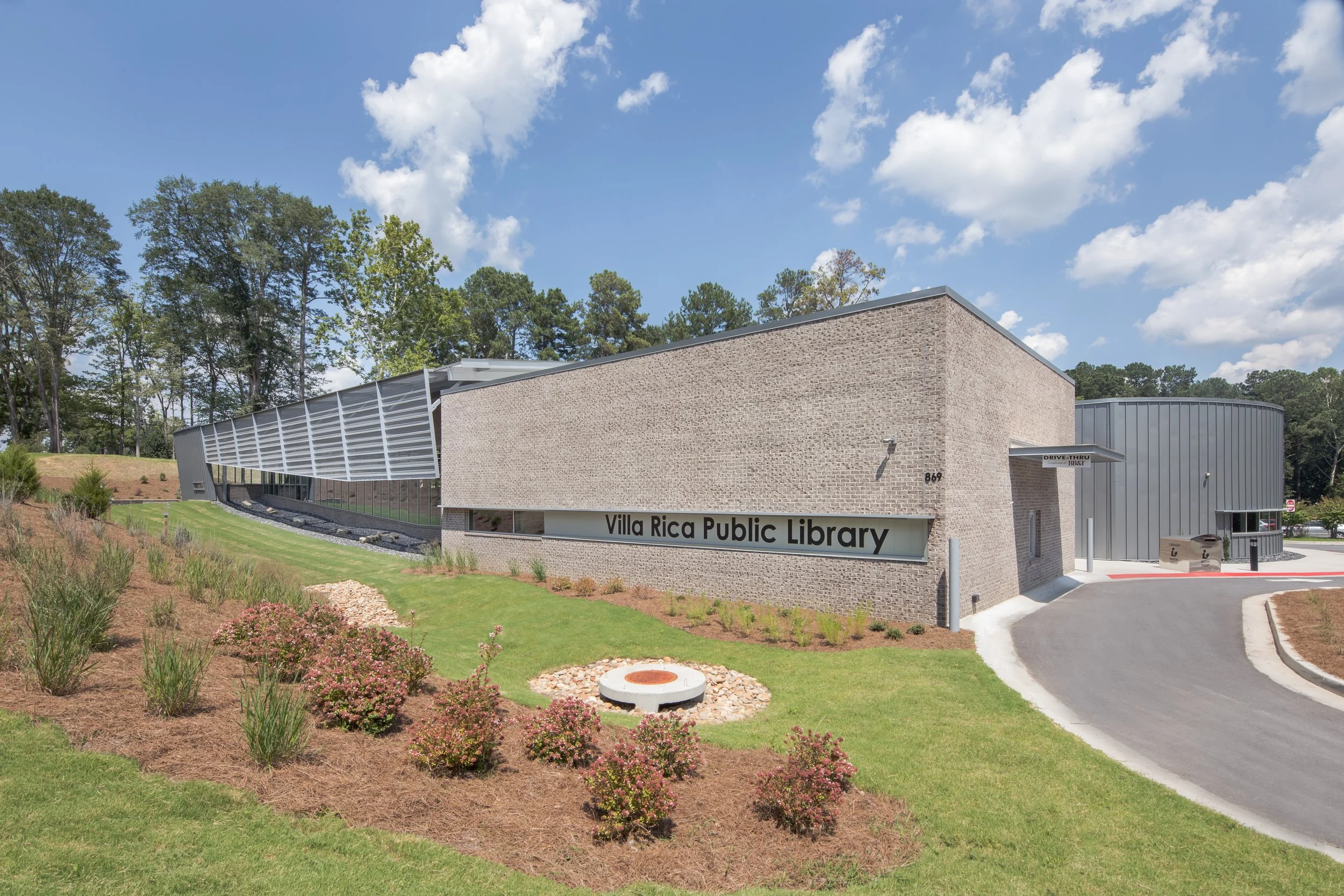 Exterior of Villa Rica Public Library with landscaped front yard, trees in background, and a partly cloudy sky.