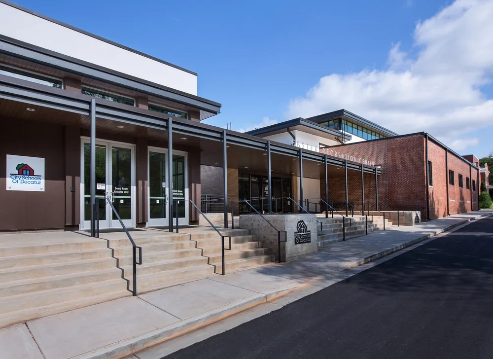 Exterior of a modern school building with steps leading to the entrance, signs for City Schools of Decatur, and Be The Change Education Center.