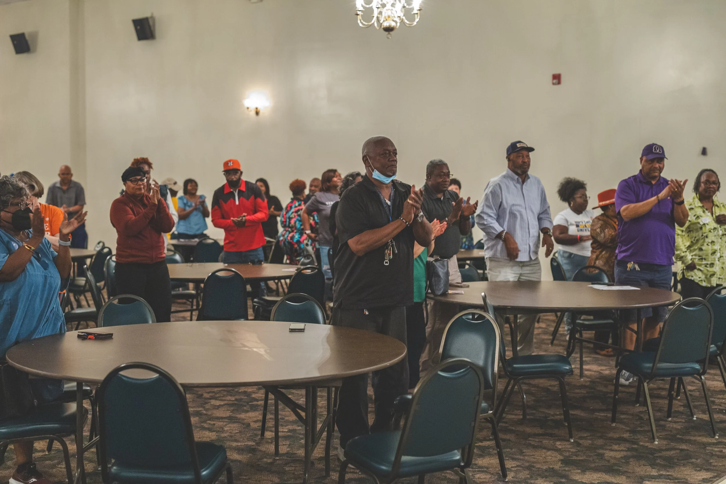 People standing in a conference room with round tables, applauding.