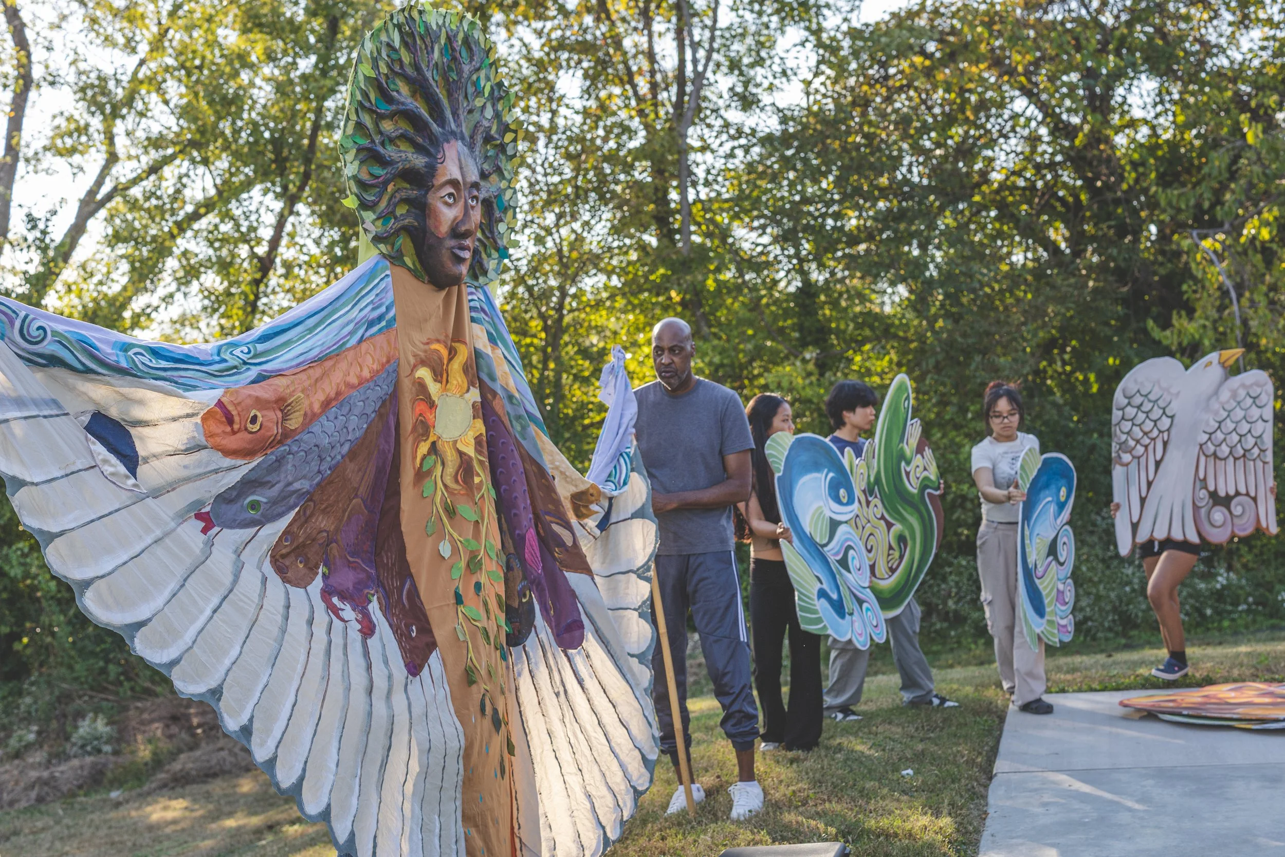 Group of people preparing and displaying large colorful kites with nature in the background.
