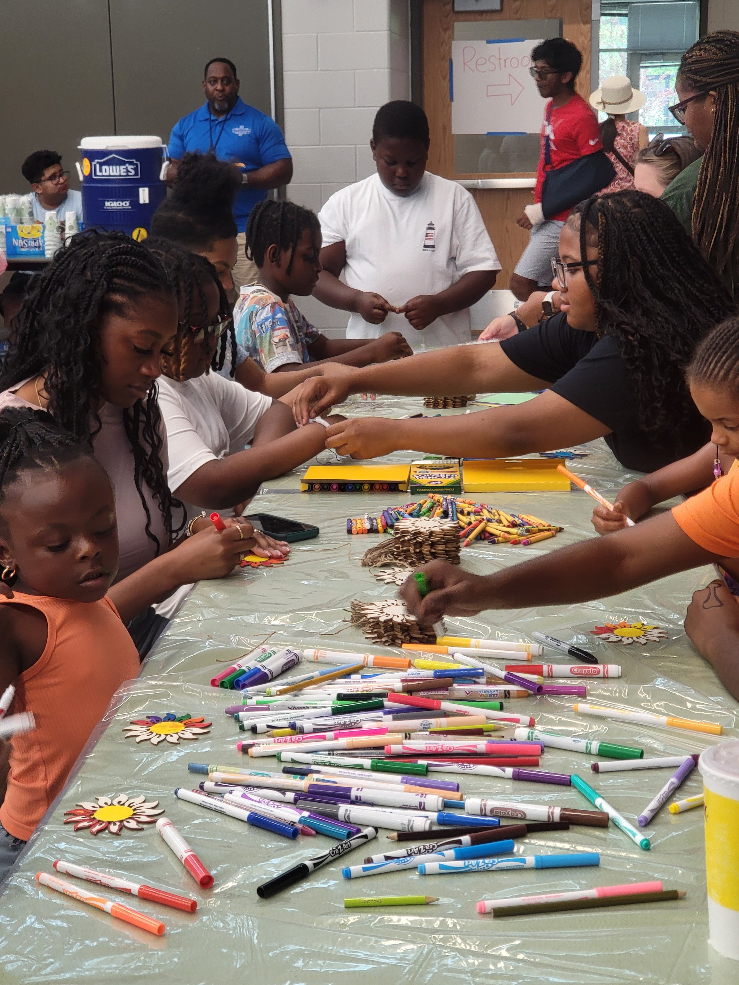 Children and adults gathered around a table decorating paper flower crafts with markers.