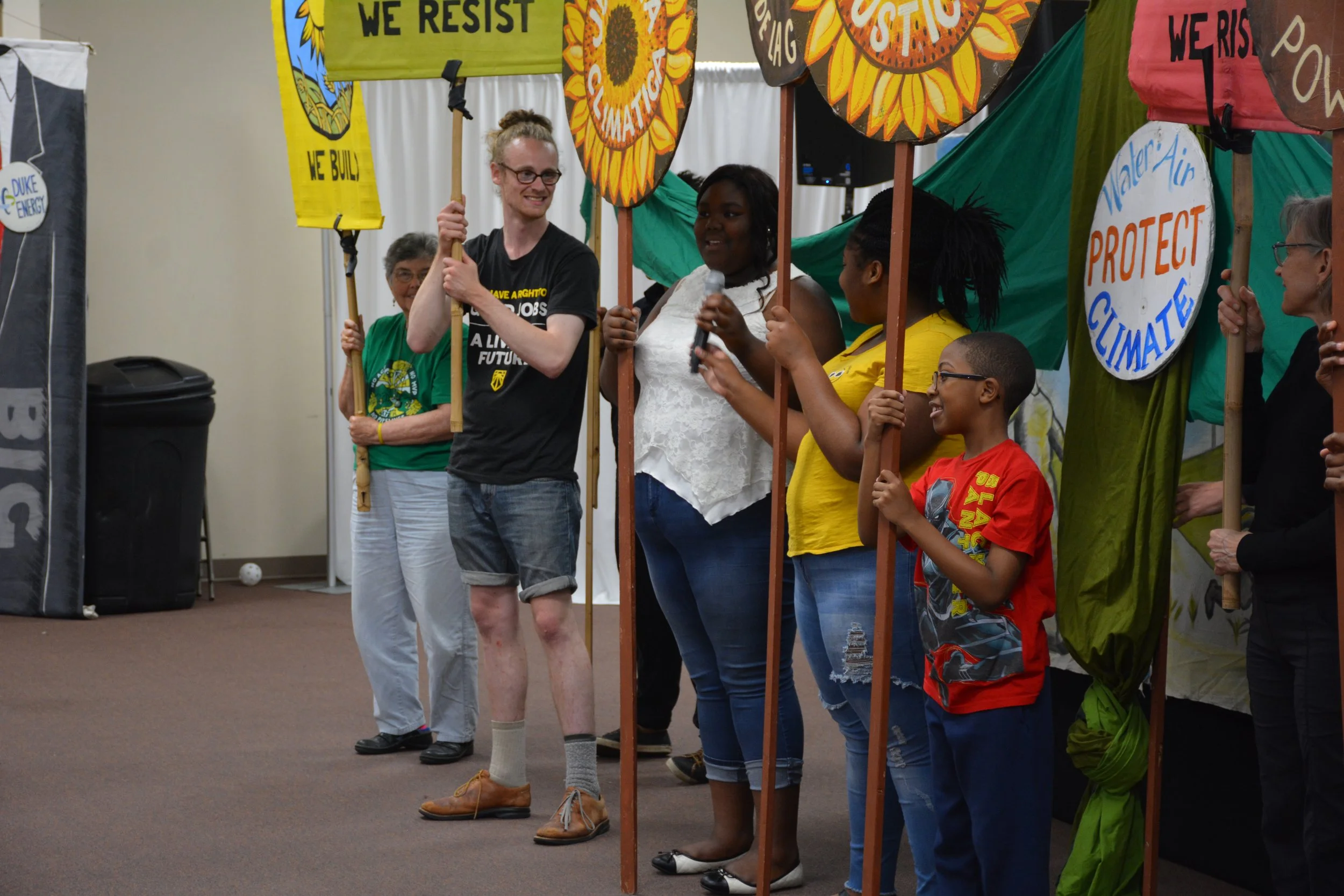Group of people participating in a climate change protest, holding signs with messages like 'We Resist' and 'Protect Climate'.