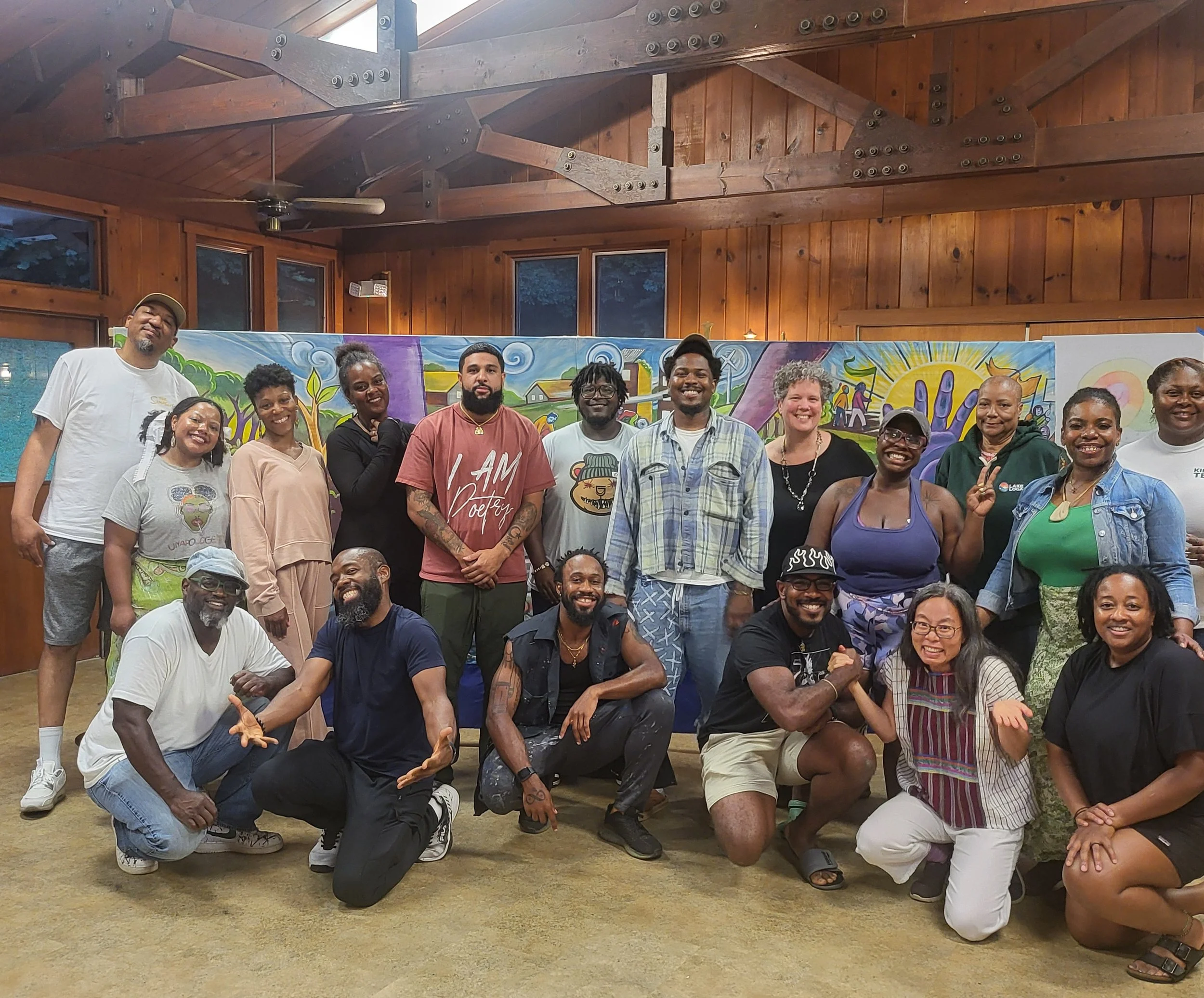 Group of diverse people posing indoors with colorful mural in the background.