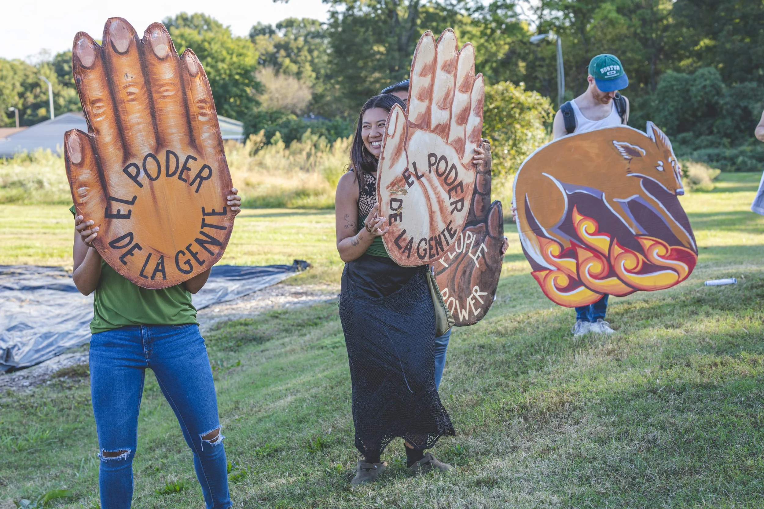 People holding large painted signs with themes of kindness and power outdoors, with trees in the background.