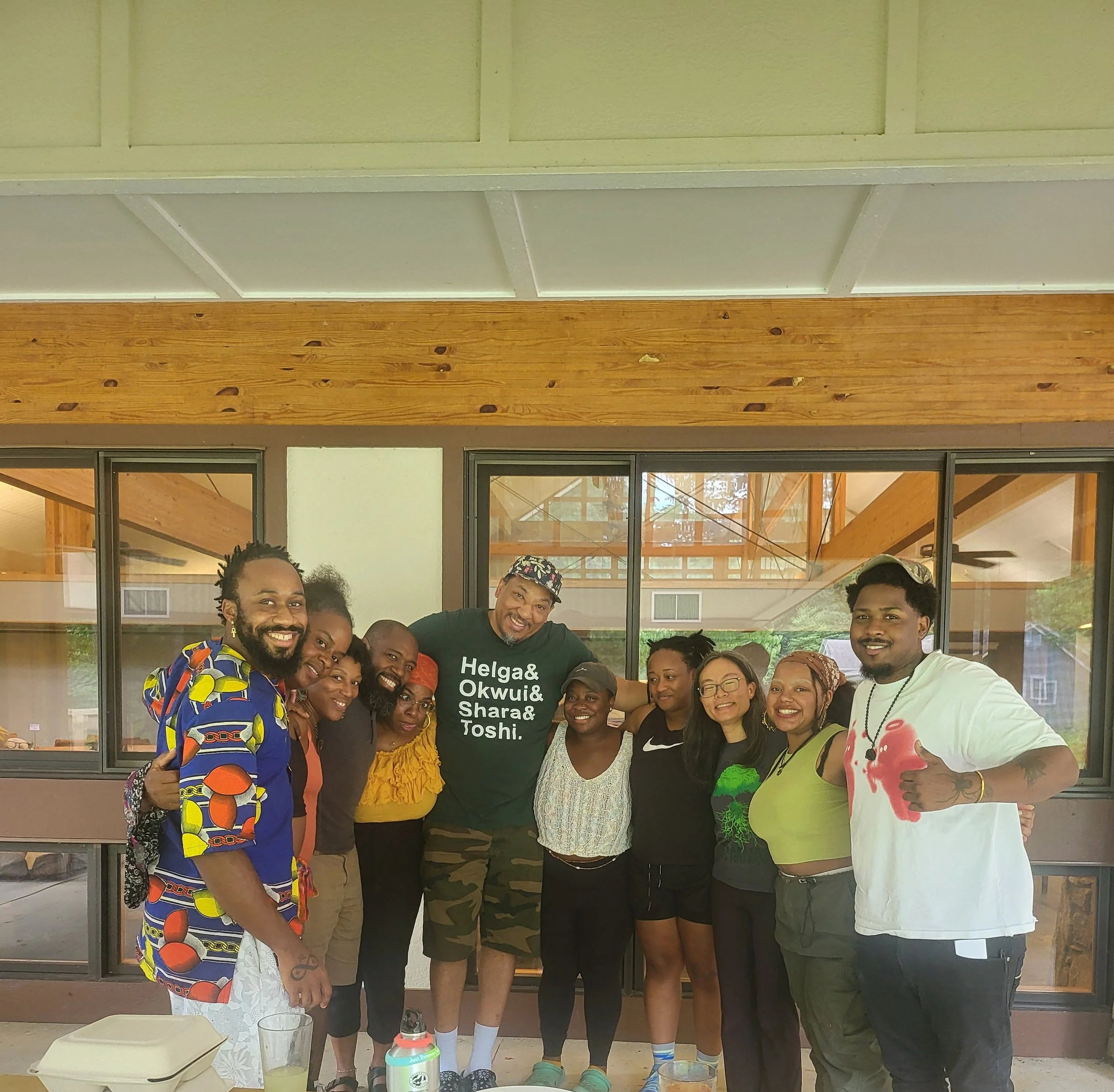 Group of ten people smiling and posing together indoors, some giving thumbs up, with wooden and glass background.