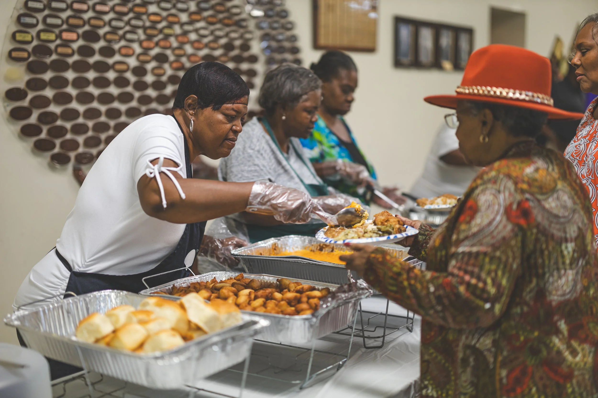Women serving food at a buffet line during a gathering.