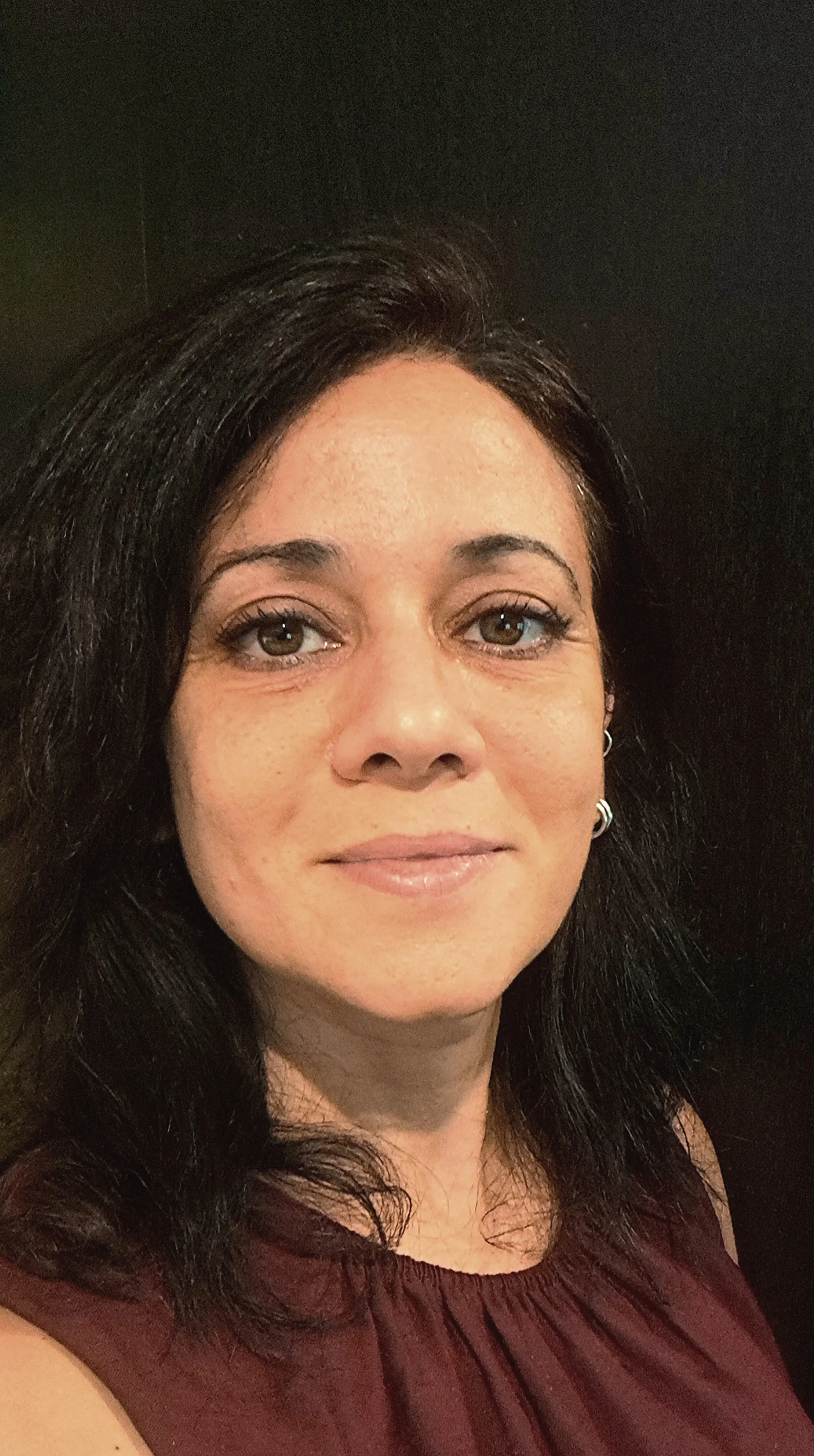 Ragazza con pelle chiara, capelli neri, indossa un top marrone e orecchini, sfondo nero.