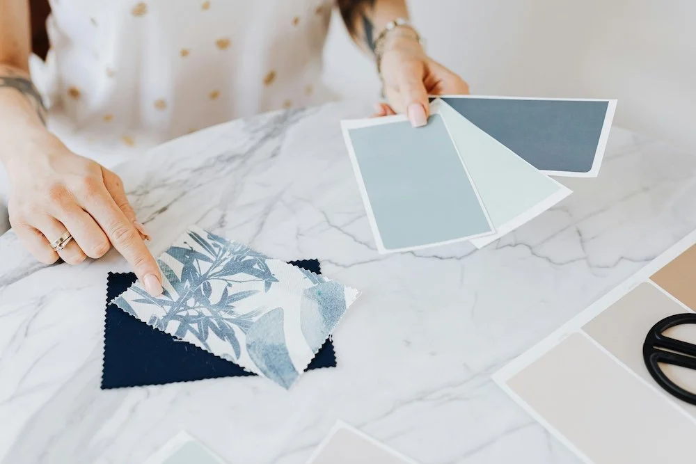 Person selecting a fabric swatch and holding color samples at a marble-detect desk.