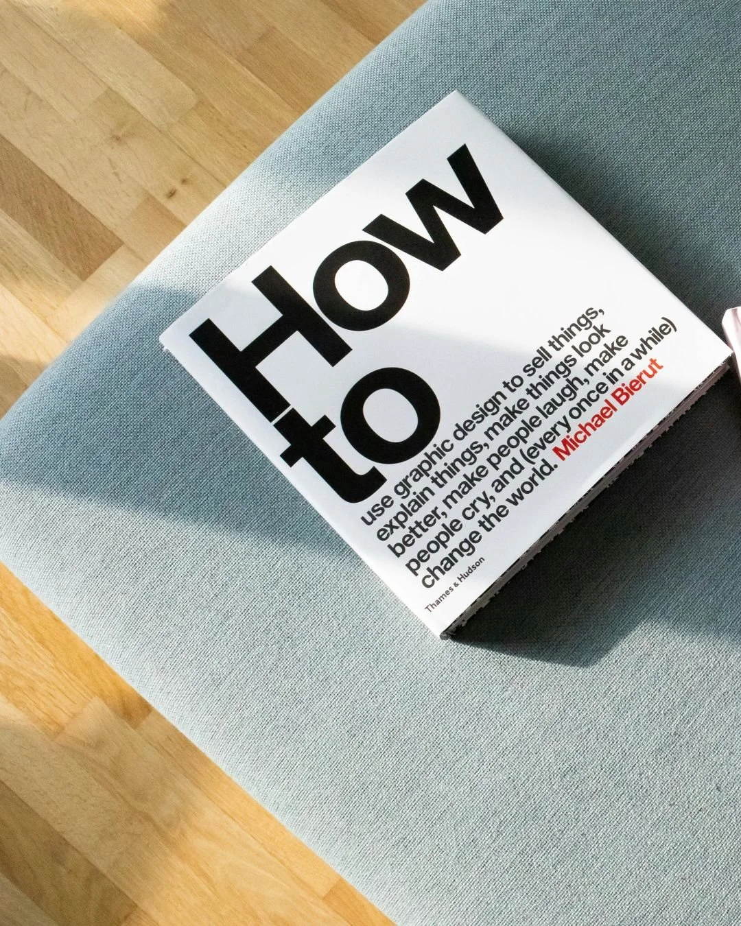 A book titled 'HOW TO' resting on a light blue fabric surface, with a hardwood floor visible in the background.