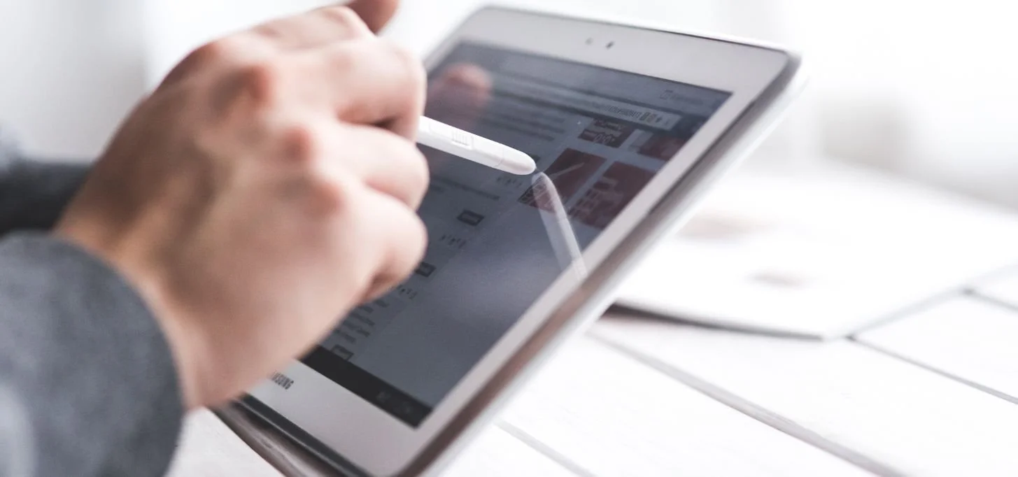 Person using a white stylus on a tablet device on a white surface.