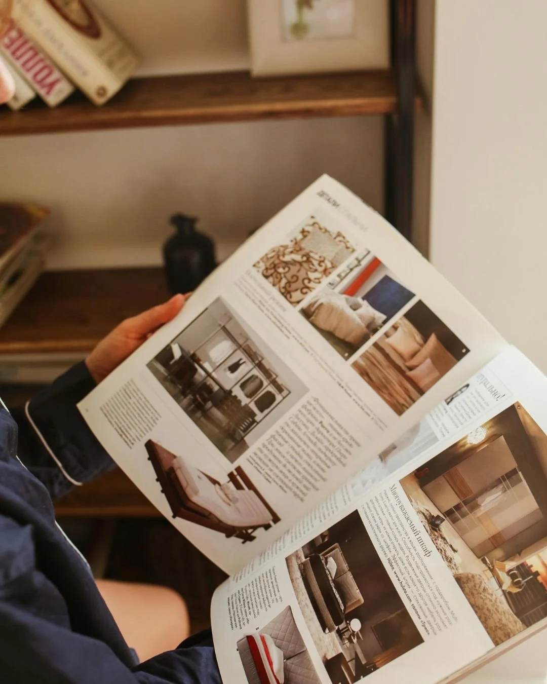 Person reading a home decor magazine with furniture and interior design images.