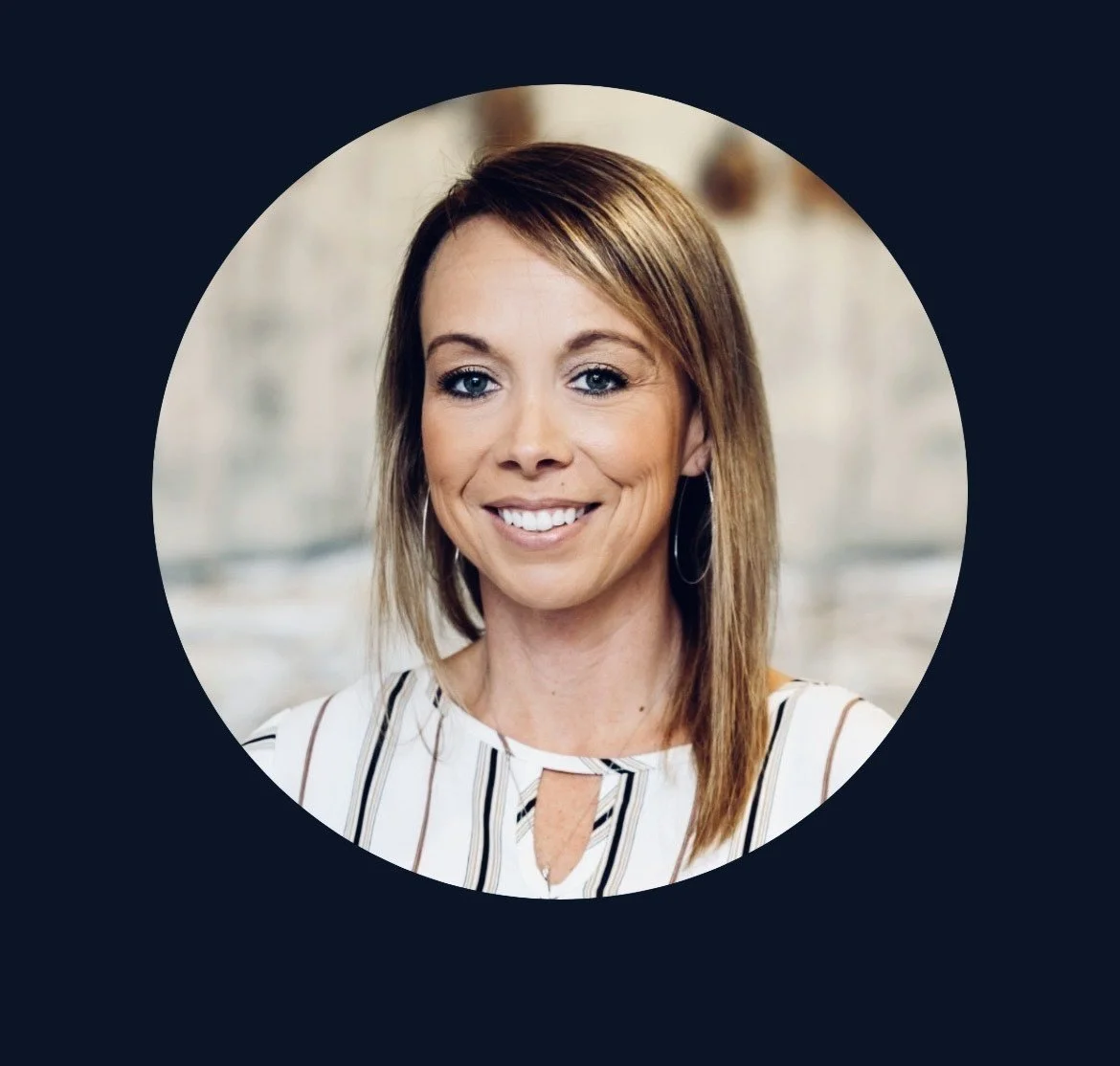 Smiling woman with shoulder-length hair and earrings, wearing a white top with black stripes, indoors with a blurred background.