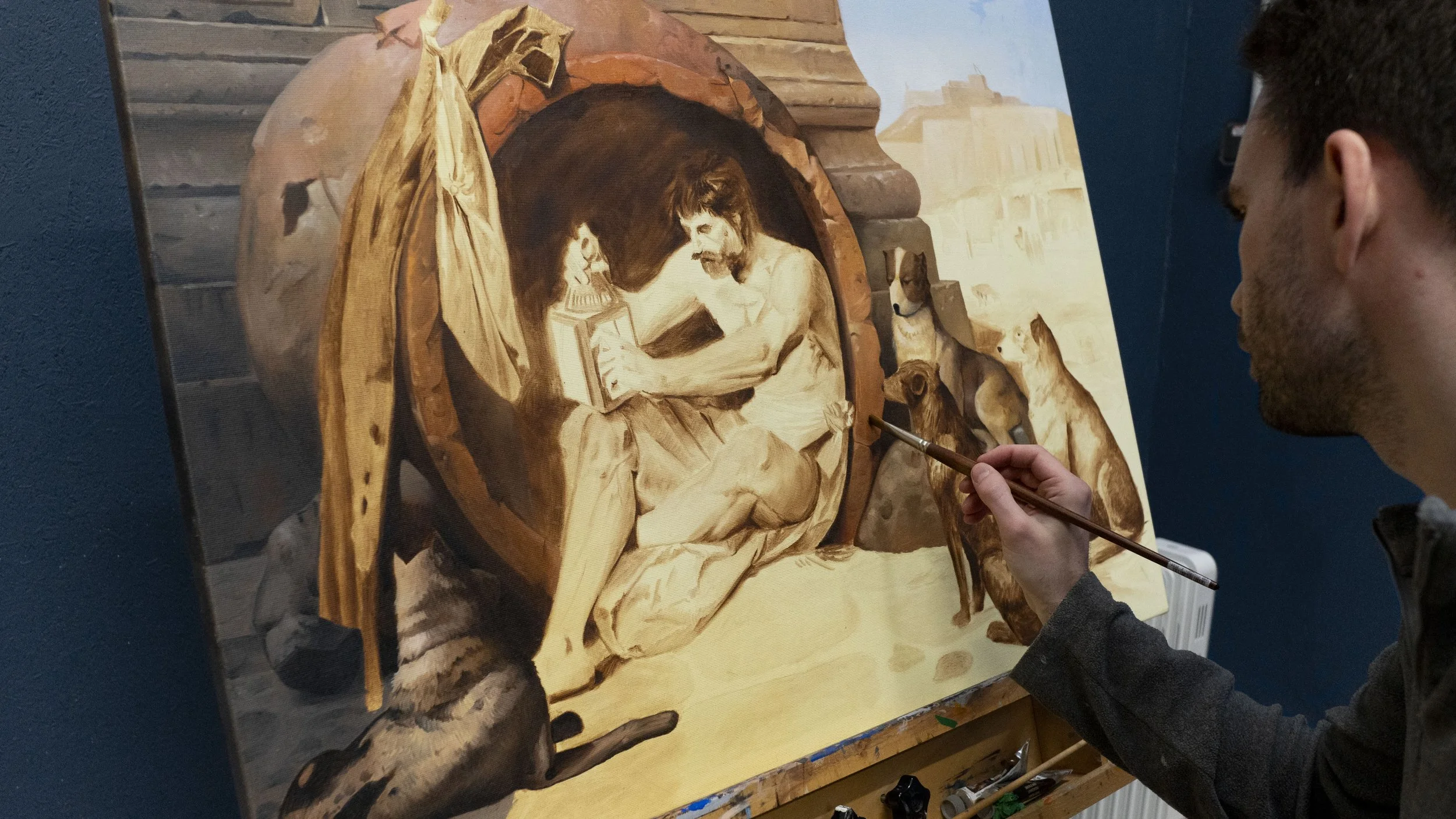 Un peintre travaille sur une toile représentant une scène de Jésus dans une armoire, entouré de chiens et d'animaux, dans un tableau en cours de réalisation.