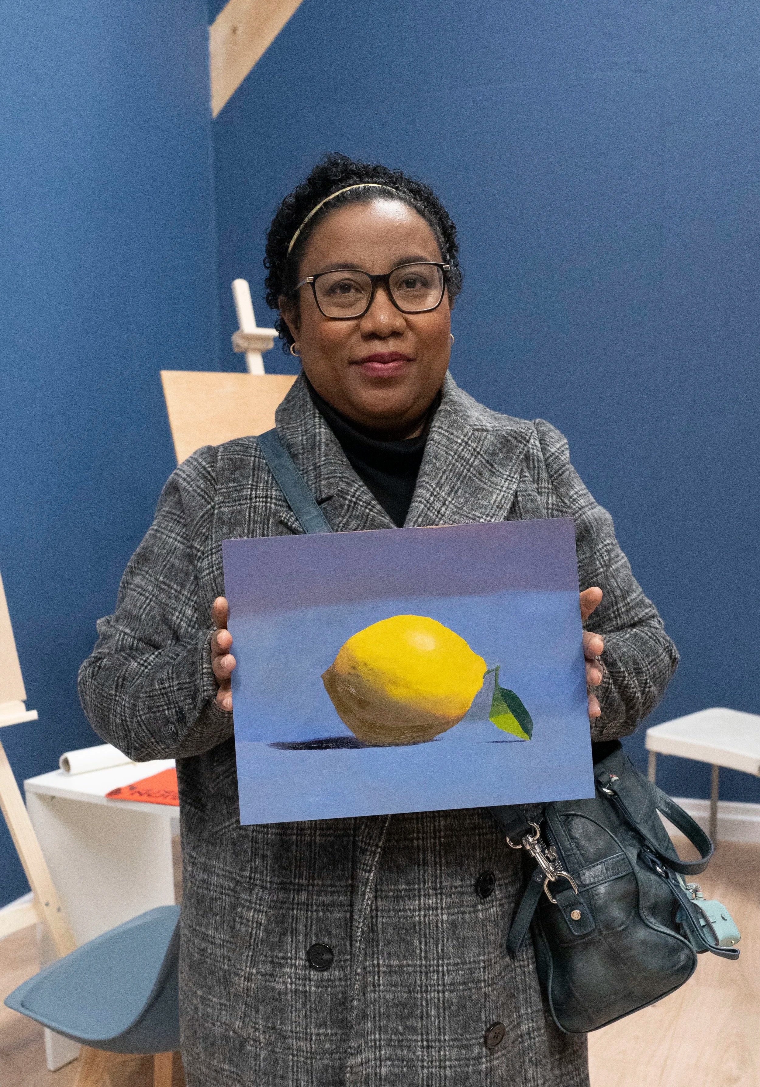 Femme tenant une peinture représentant un citron sur fond bleu dans une salle d'exposition.