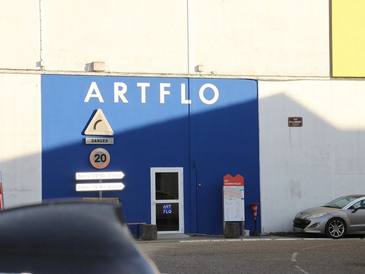 Un bâtiment bleu avec le nom ART FLO écrit dessus, une porte d'entrée, des panneaux de signalisation, et une voiture garée à côté.
