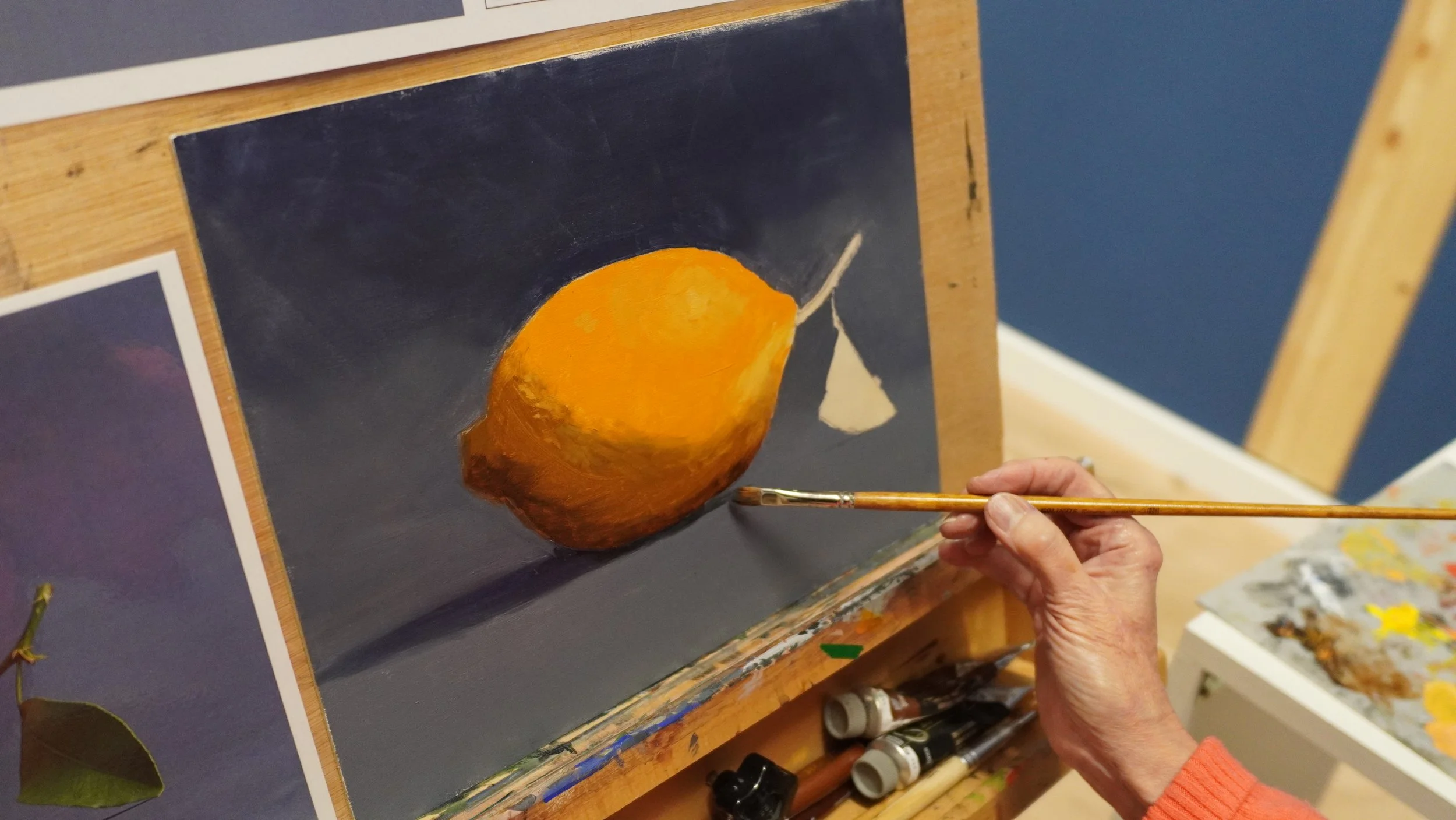 Peinture à l'huile d'un citron sur un fond sombre, avec une palette visible à droite, en train d'être peinte par un artiste.