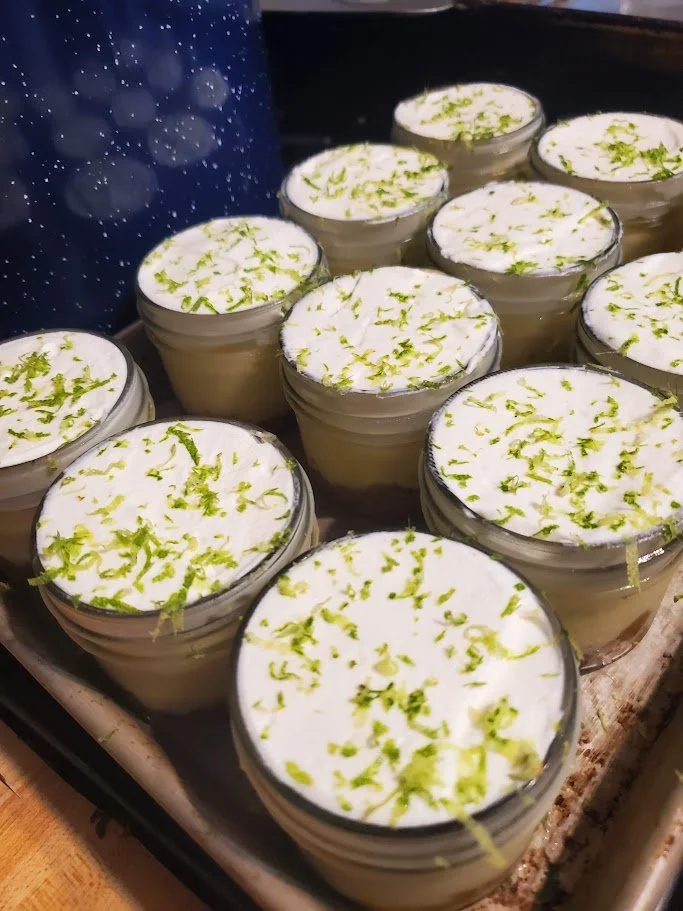 Multiple small glass cups filled with a creamy dessert, topped with lime zest, arranged on a tray.