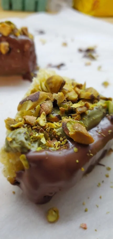 Close-up of a pistachio-topped chocolate and brown butter rice crispy treat slice on parchment paper.