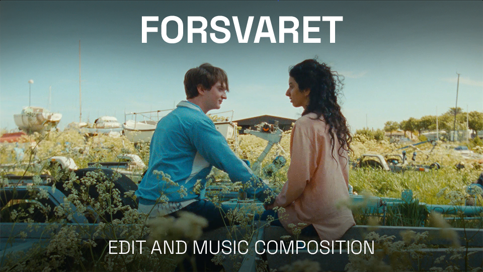 A young man and woman sitting on a boat in a field of wildflowers, holding hands and looking at each other, with a marina and boats in the background.