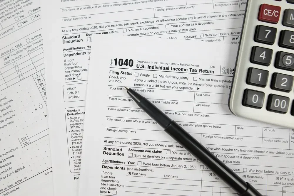 Close-up of a 1040 U.S. individual income tax return form, with a black pen placed on it, near the edge of a calculator and another tax form in the background.