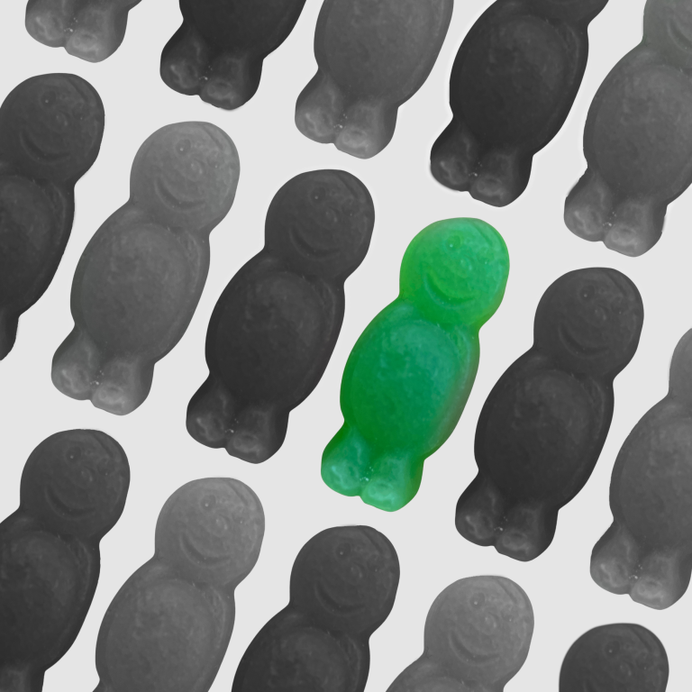 A green gummy bear with a smiling face surrounded by black and white gummy bears.