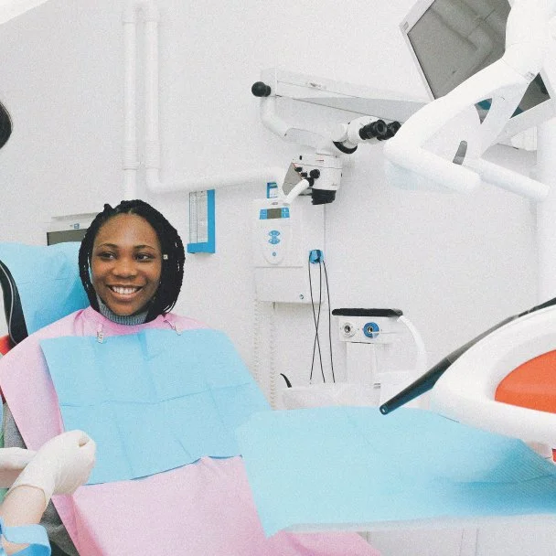 Smiling woman in a dental chair with dental equipment and light overhead in a dental clinic.
