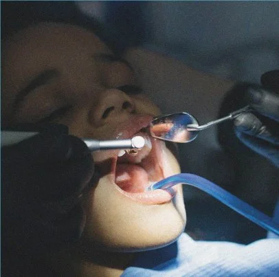 A person undergoing a dental examination with a mirror and dental tools in their mouth.