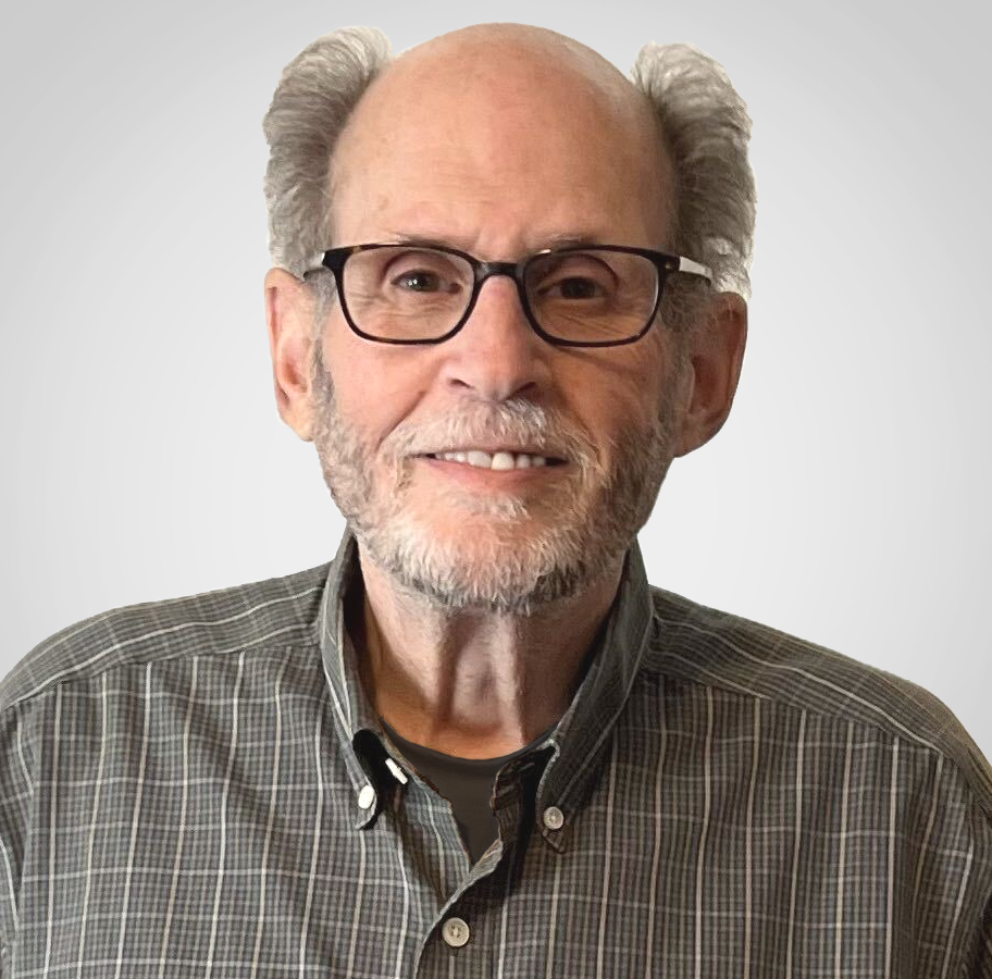 A smiling HR expert with glasses, gray hair, and a beard, wearing a plaid shirt against a plain light gray background.